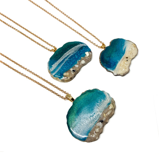 Three necklaces with ocean-inspired pendants, featuring blue resin and sand-like textures.