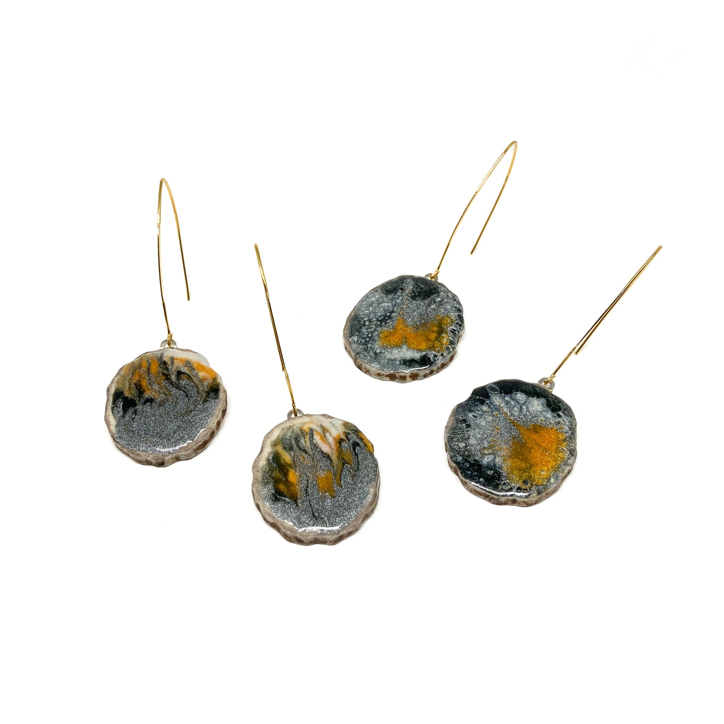 Four round earrings with black, white, and gold abstract designs, featuring gold hooks.