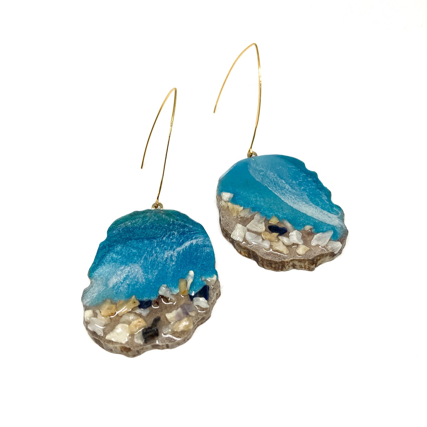 Two round earrings with blue resin and sand-like textures, featuring gold hooks. Ocean-inspired design.