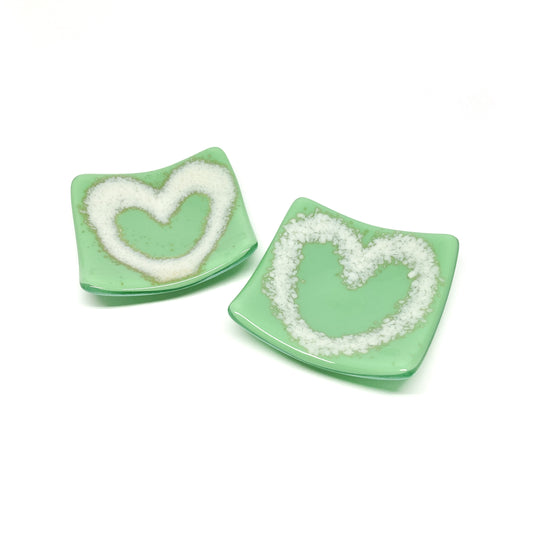 Two fused glass heart bowls, one with a white heart on a green base, the other similar.