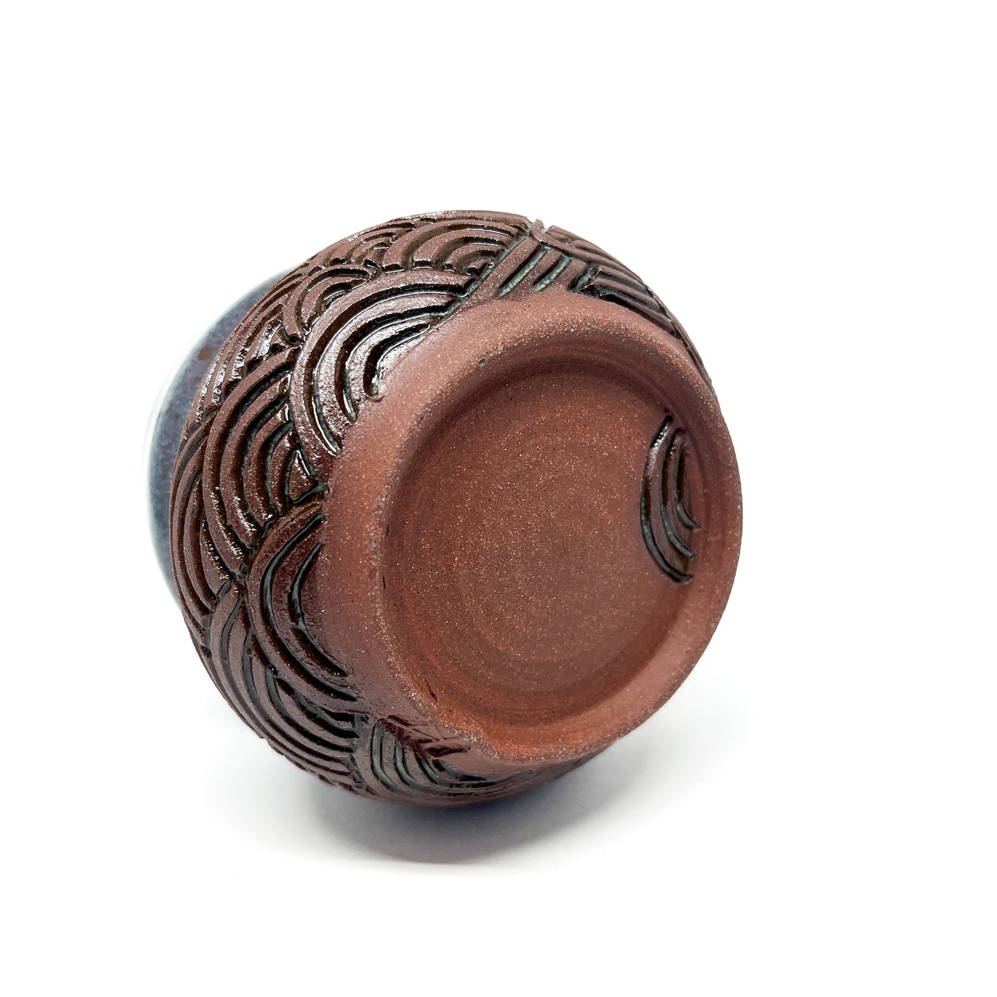 A small, carved ceramic cup with a blue-green top and a brown bottom featuring a wave design.