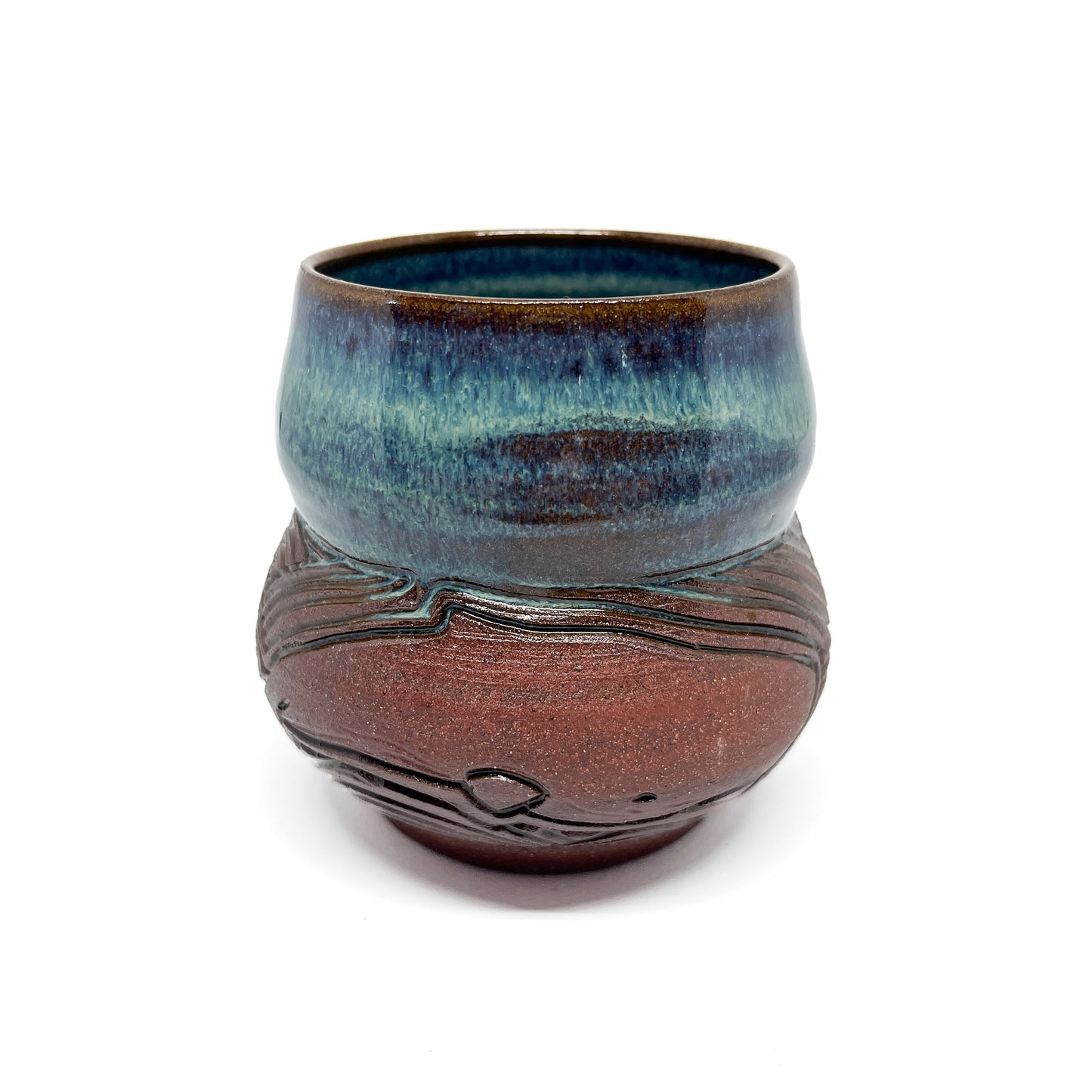A small, carved ceramic cup with a blue-green top and a brown bottom featuring a carved whale design.
