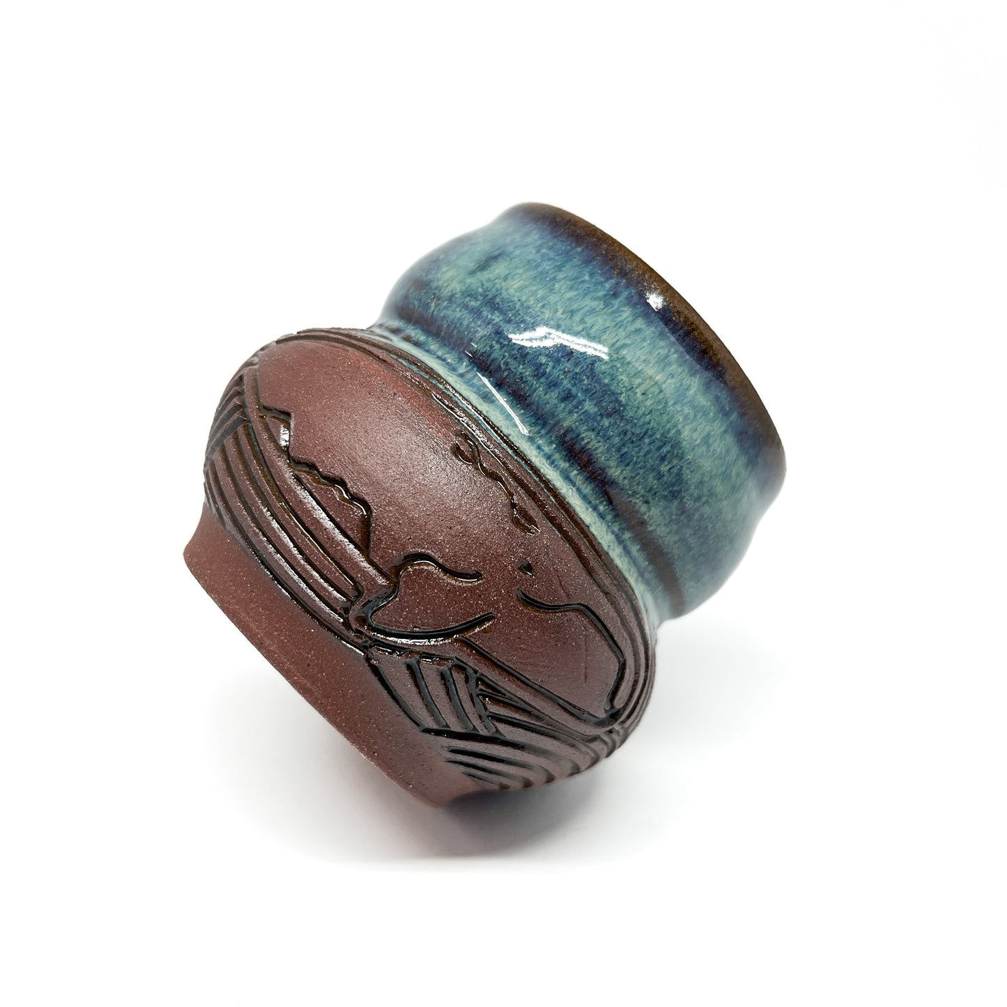 Small ceramic cup with a carved whale design on a textured brown base and a glossy blue-green rim.