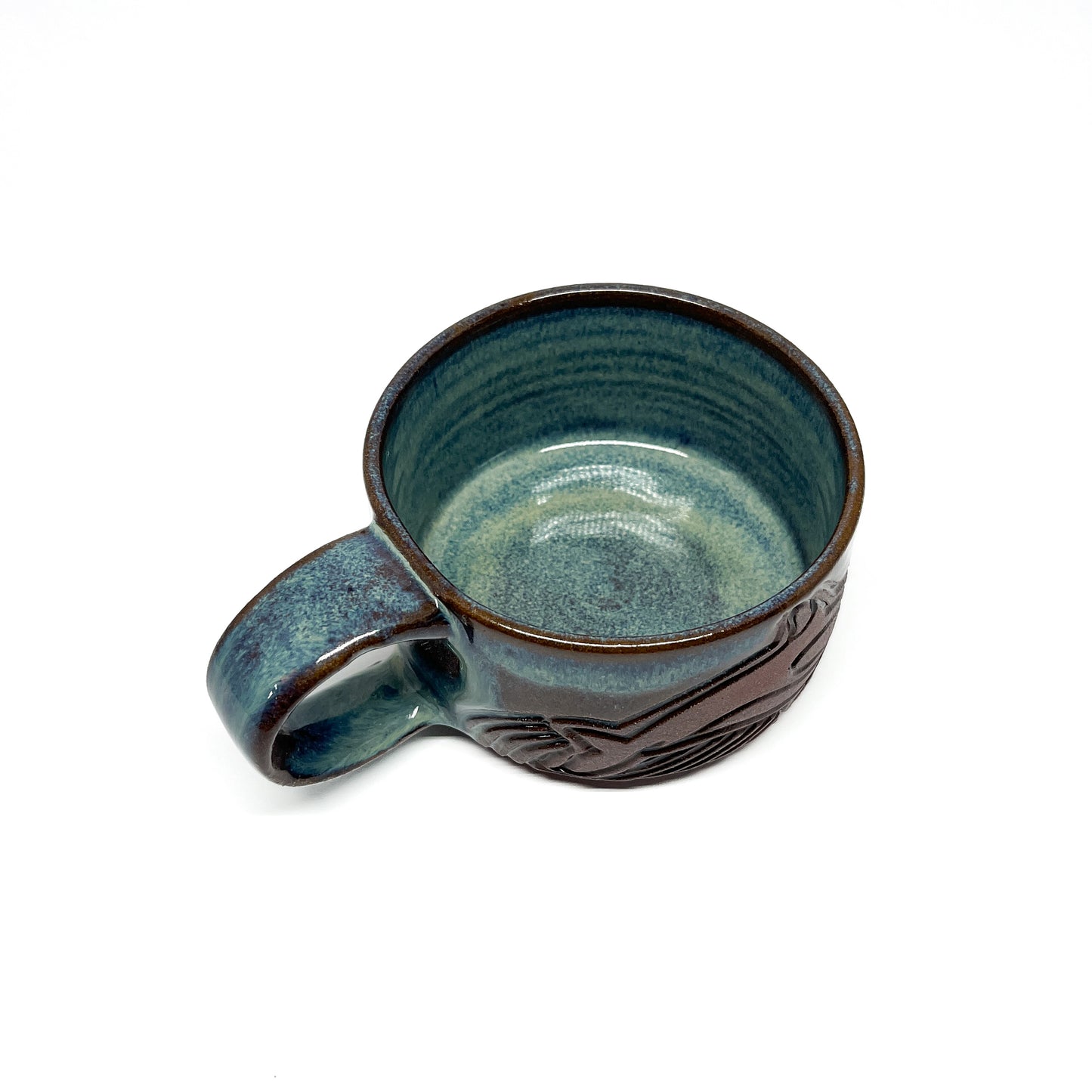 Ceramic mug with a carved whale and wave design in brown against a glossy blue-green glaze and a rounded handle.
