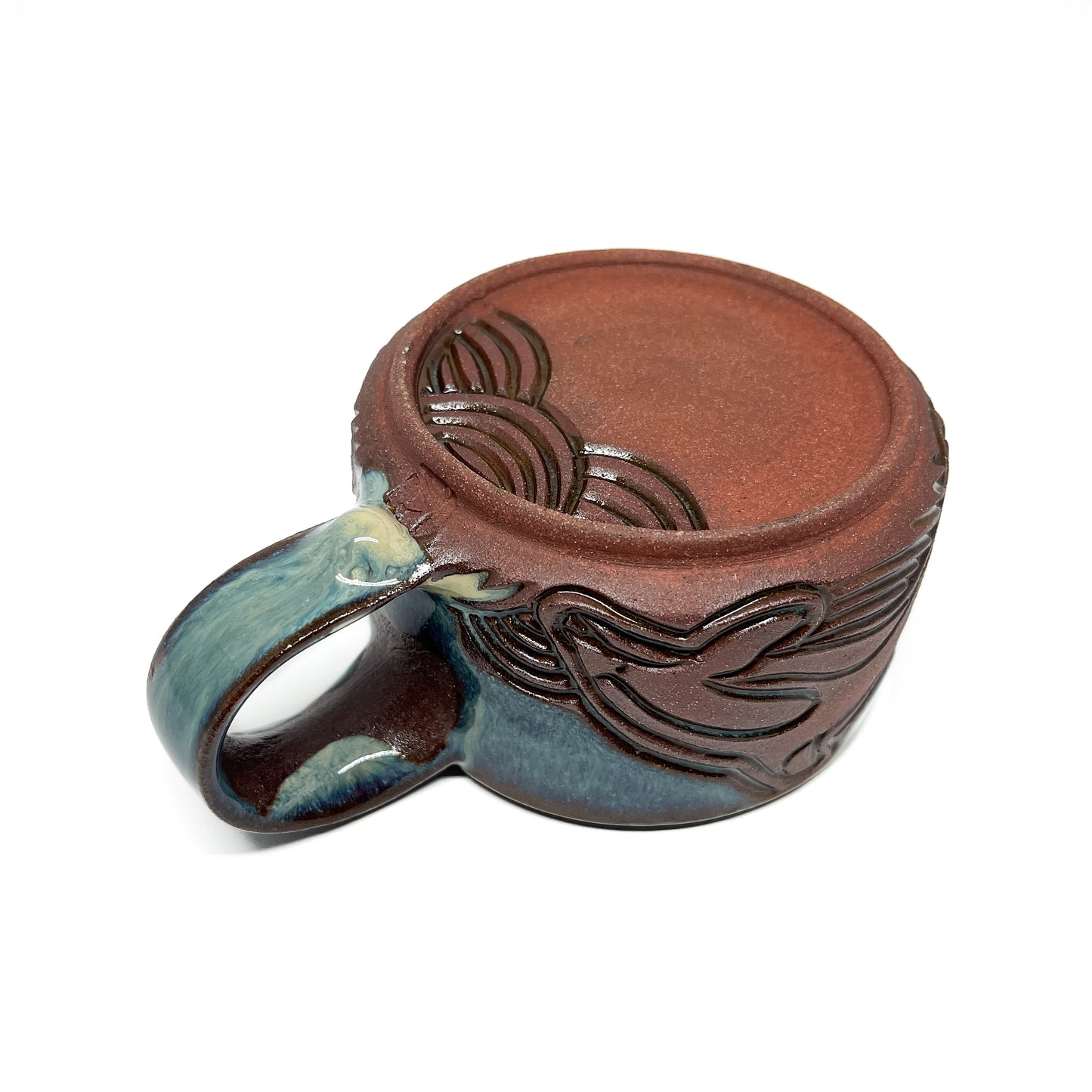 Handmade ceramic mug with carved wave design and blue-green handle.