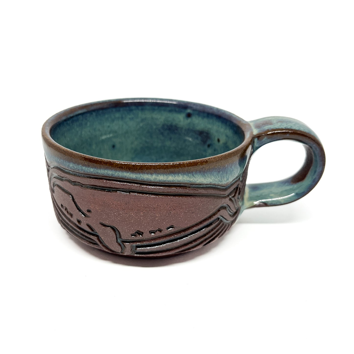 Handcrafted ceramic cup with a whale and wave motif, featuring a smooth glaze and a rounded handle.