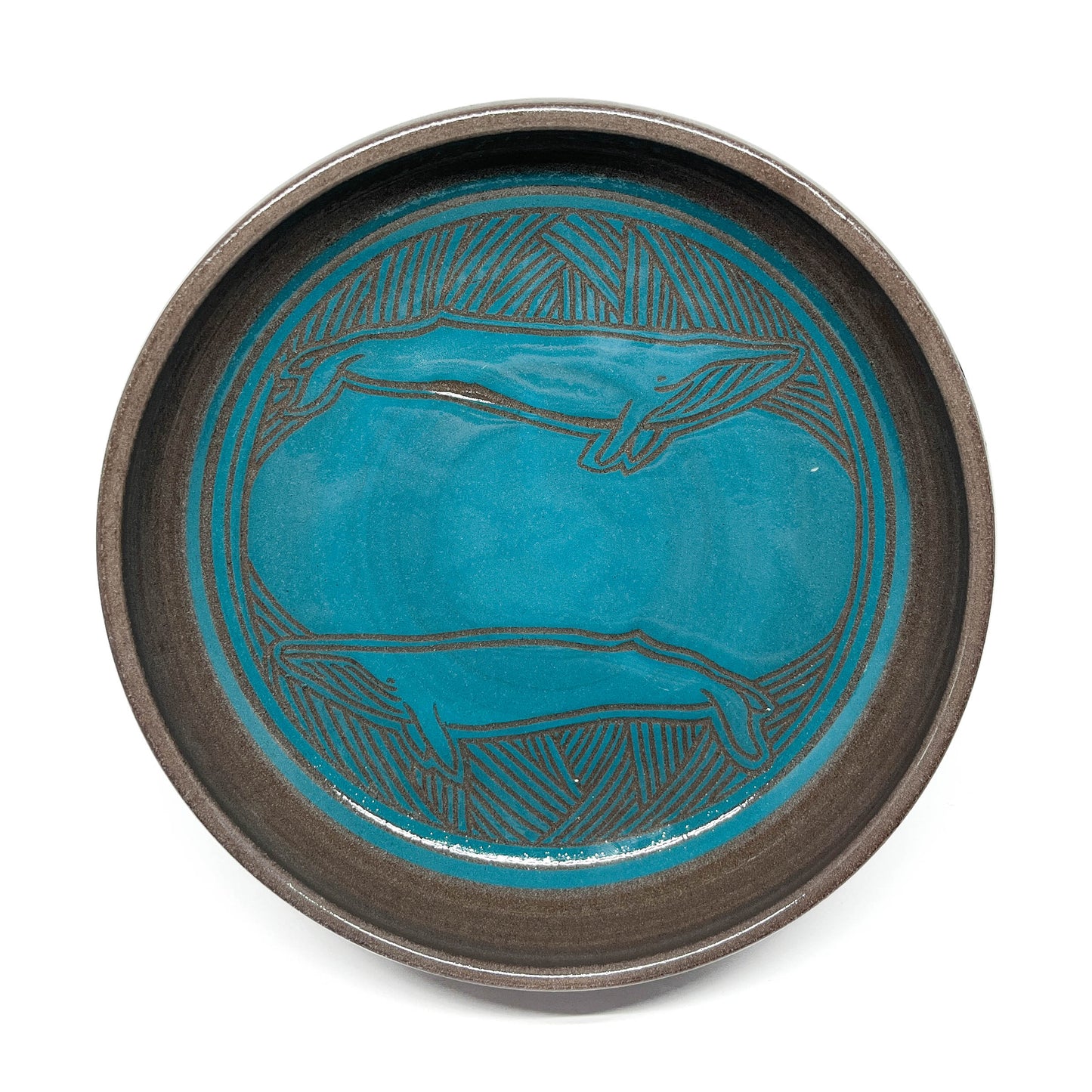 A teal ceramic bowl with an engraved pattern sits on four feet.