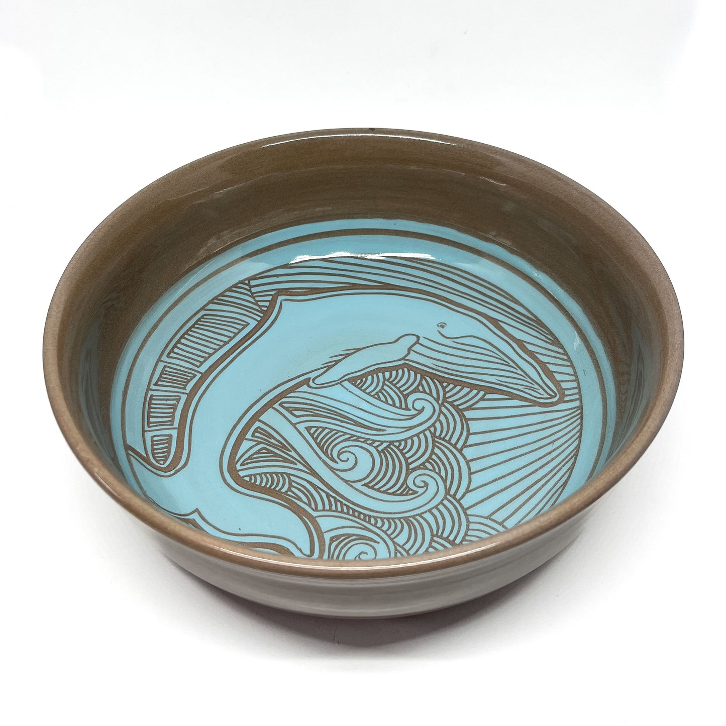 Ceramic bowl featuring a carved humpback whale design surrounded by swirling lines and radiant beams.