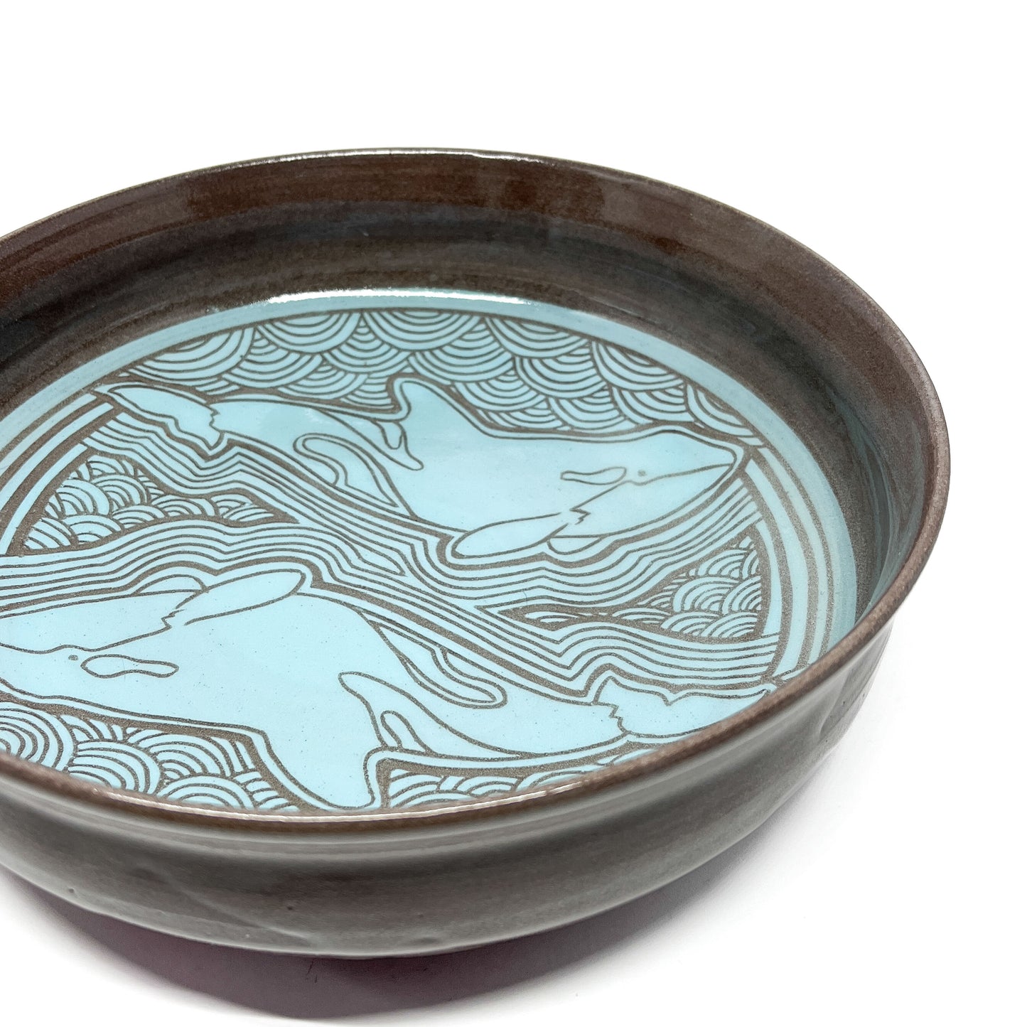 Bowl with two stylized whales swimming among waves and surrounded by circular line patterns.