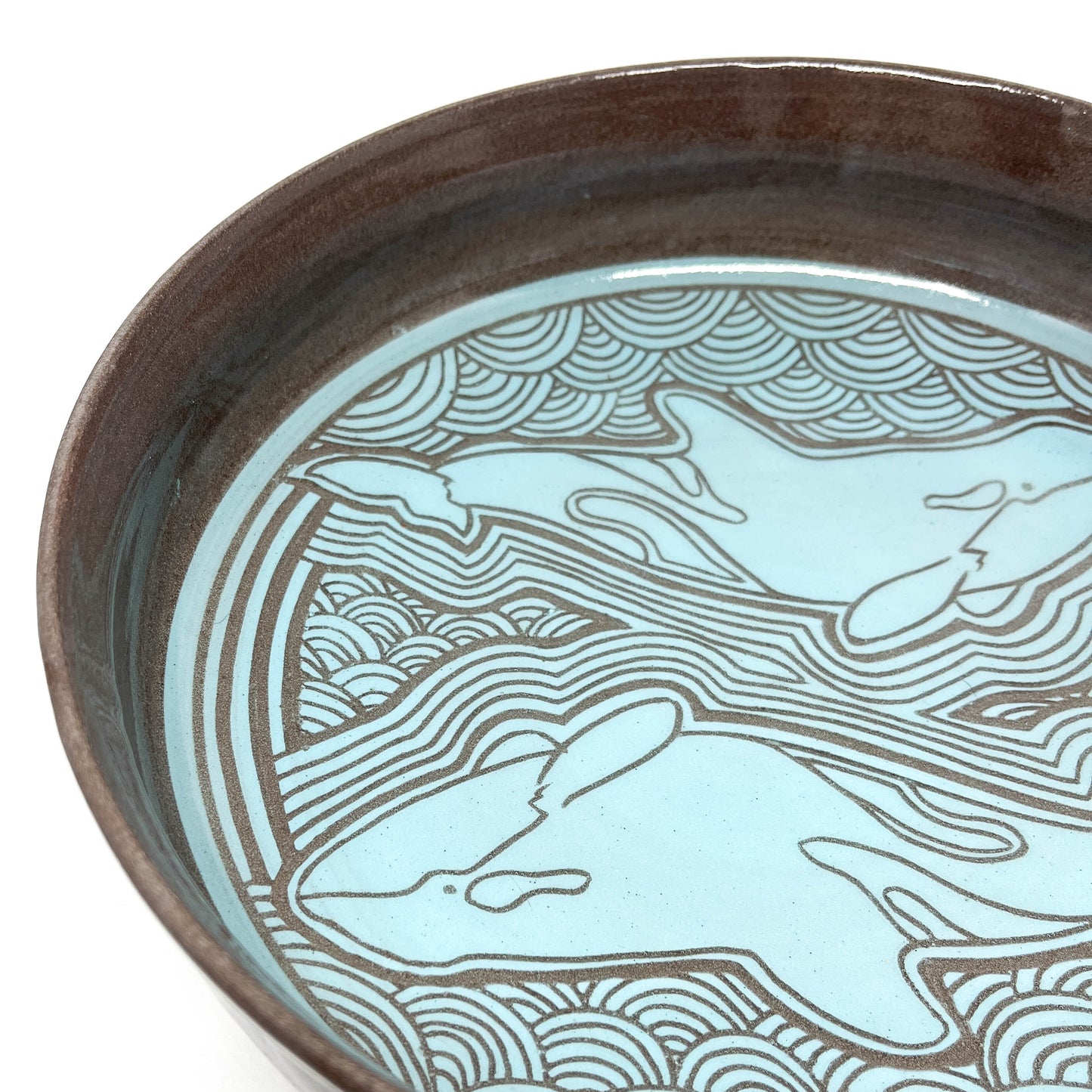 Overhead view of a bowl featuring a single whale surrounded by radiating lines and stylized waves.