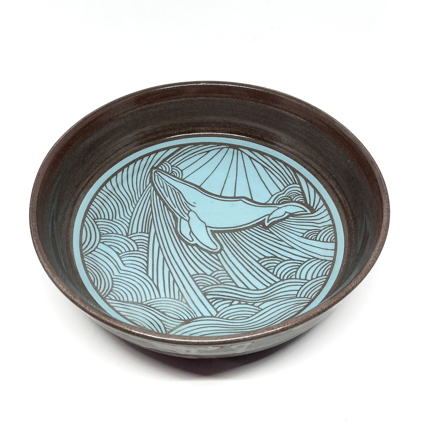 Angled top view of a bowl with a whale swimming through stylized waves and rays in the background.