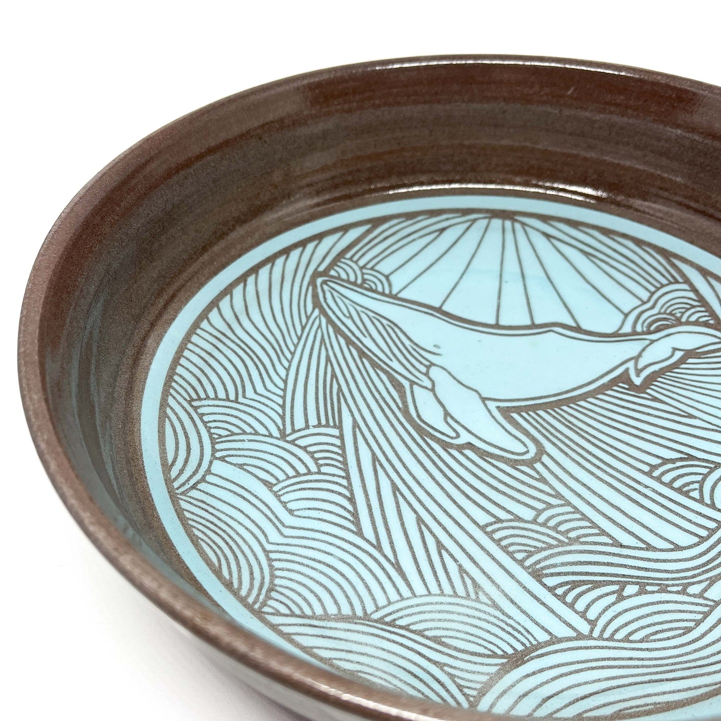 Close-up of a ceramic bowl featuring an engraved whale design surrounded by stylized waves and sun rays.