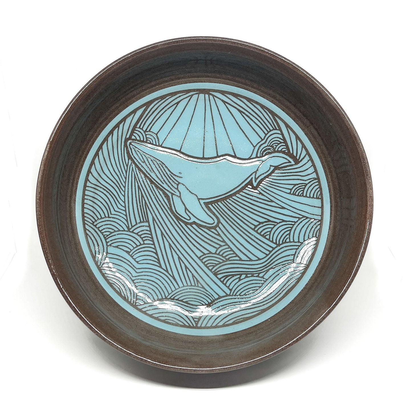 Top view of a ceramic bowl featuring an etched whale surrounded by stylized waves and radiating lines.