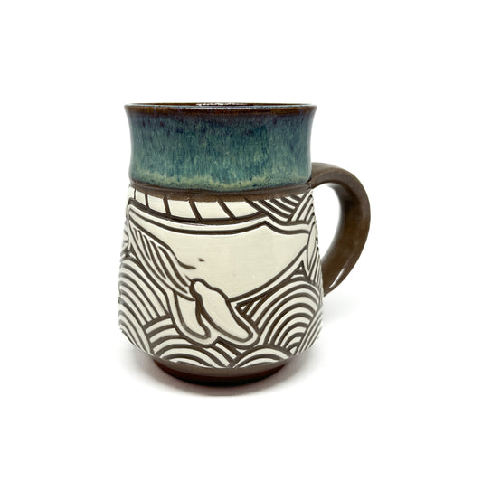 Handmade ceramic mug with a carved whale and wave design, featuring a textured, glazed upper rim.
