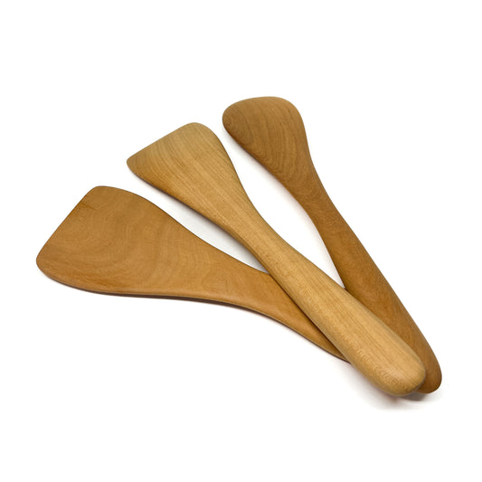 Three wooden spatulas in varying shades, angled on a white surface.