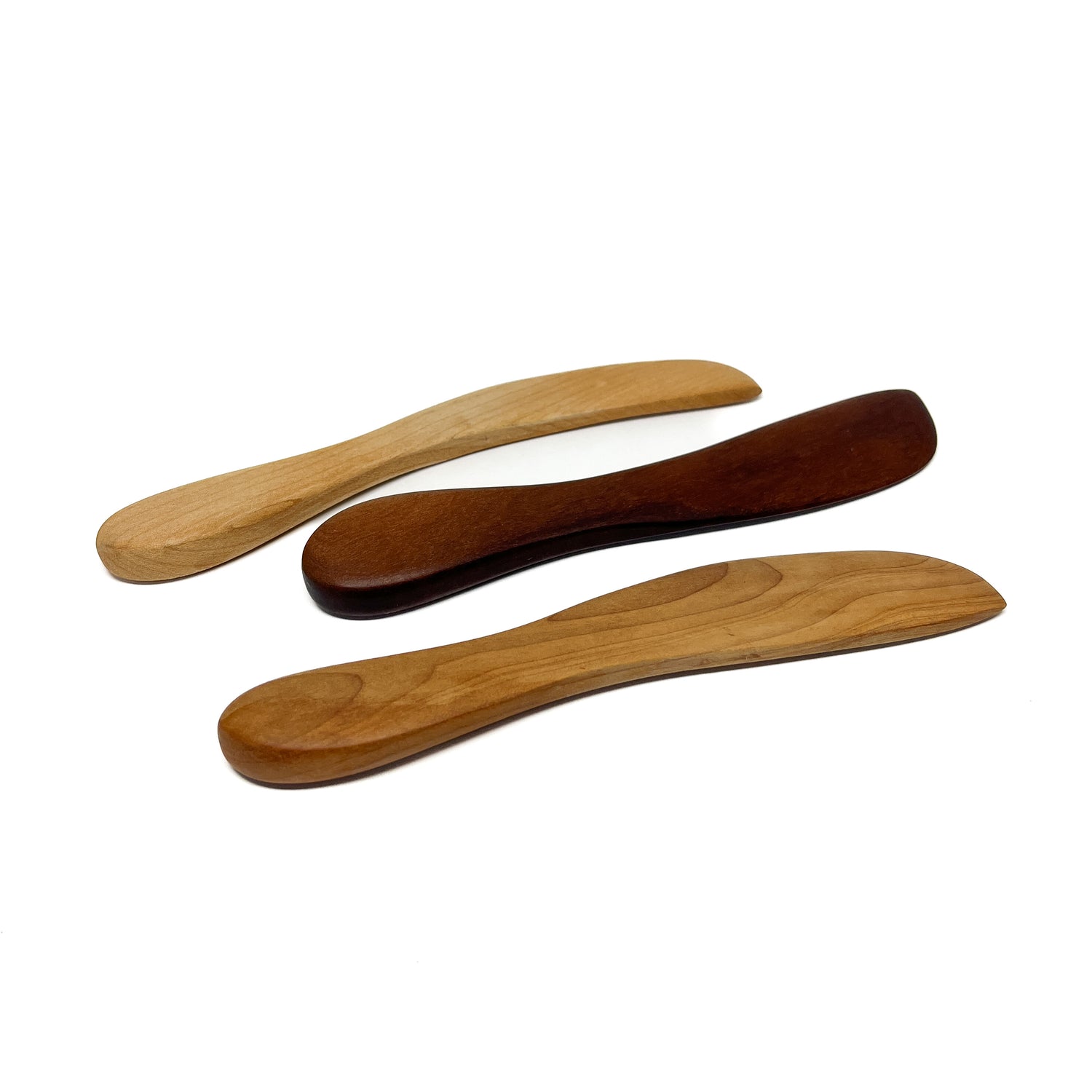 Three wooden spread knives in varying shades, angled on a white surface.