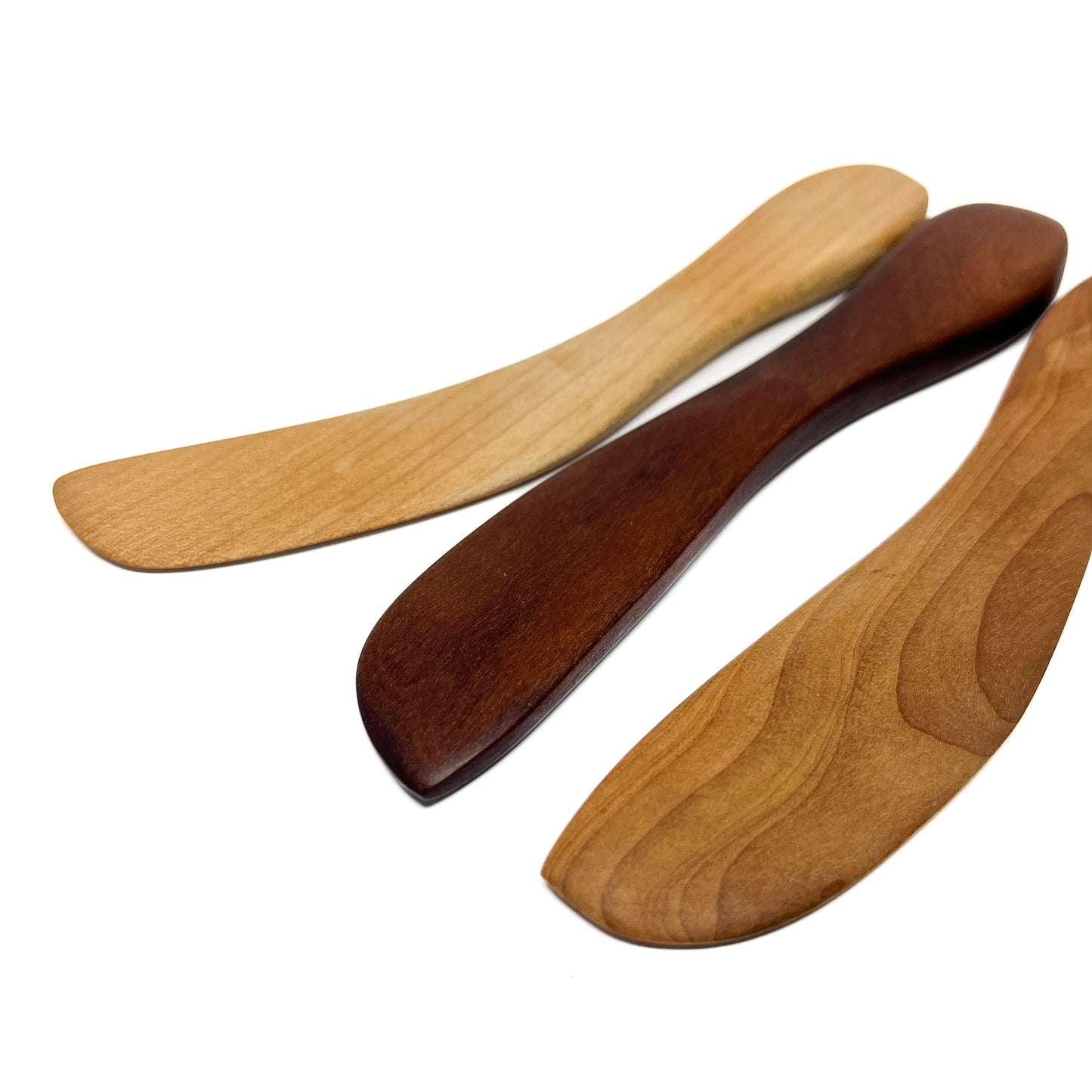 Three wooden spread knives in varying shades, angled on a white surface.