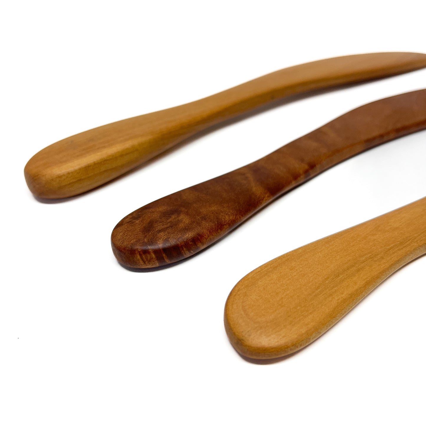 Three wooden spread knives in varying shades, angled on a white surface.