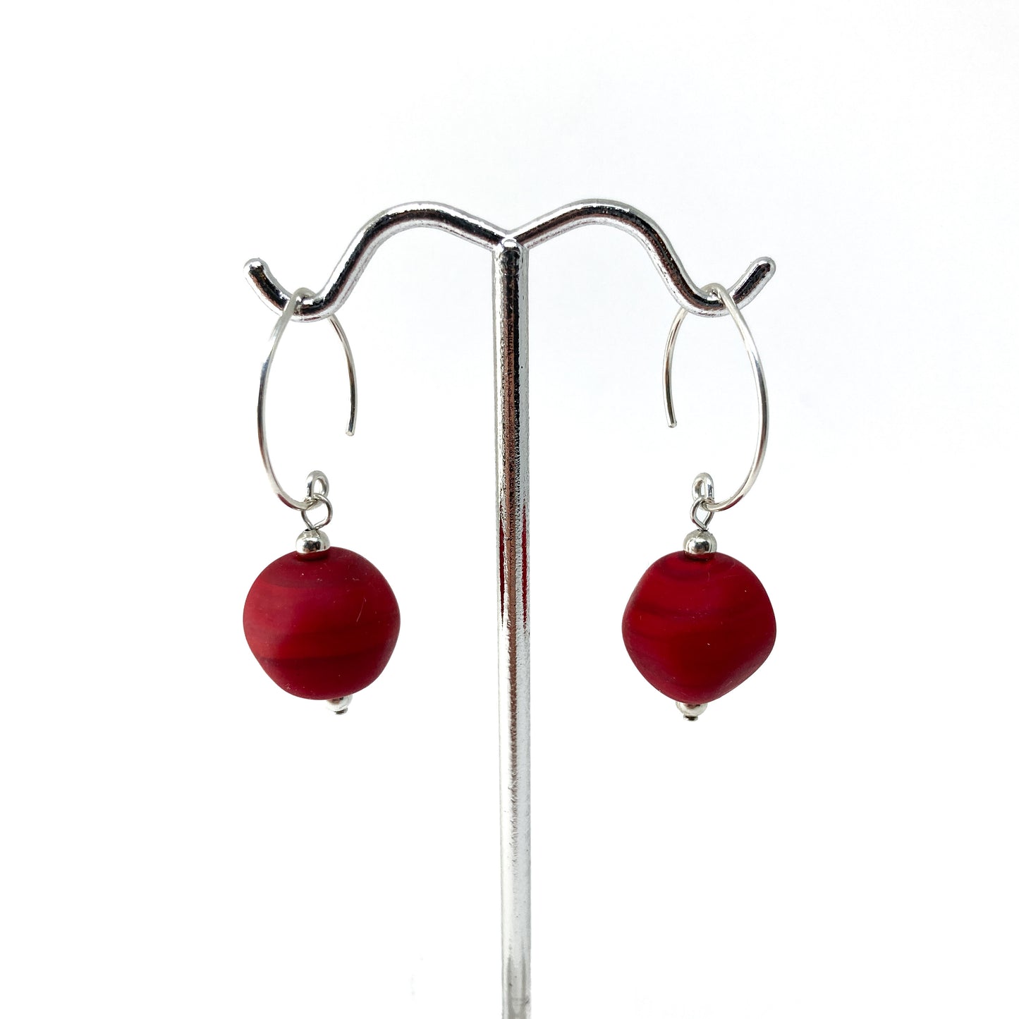 A pair of earrings with red glass beads hanging from silver hoops on a metal stand.