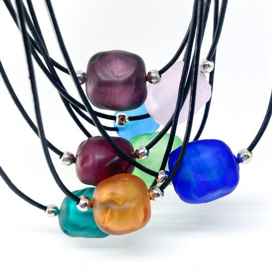 Multiple black cord necklaces with various colored beads and silver accents.