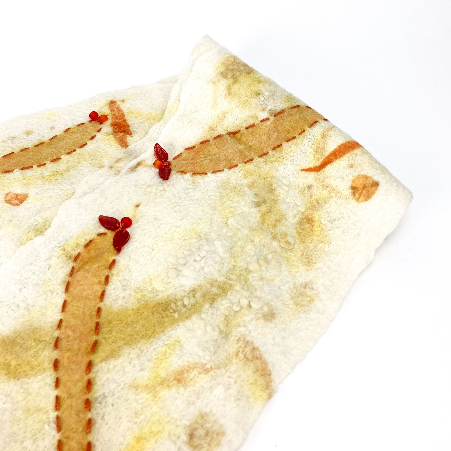 Textured eco-print scarf featuring stitched orange shapes, faded yellow marks, and tiny red accents.