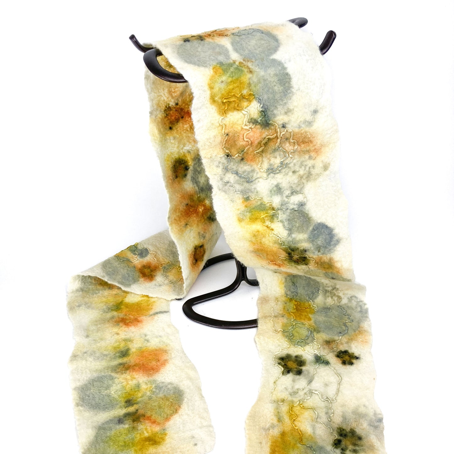 Eco Print Scarf draped on a black stand. The off-white scarf features organic shapes in muted yellows, greens, and soft oranges.