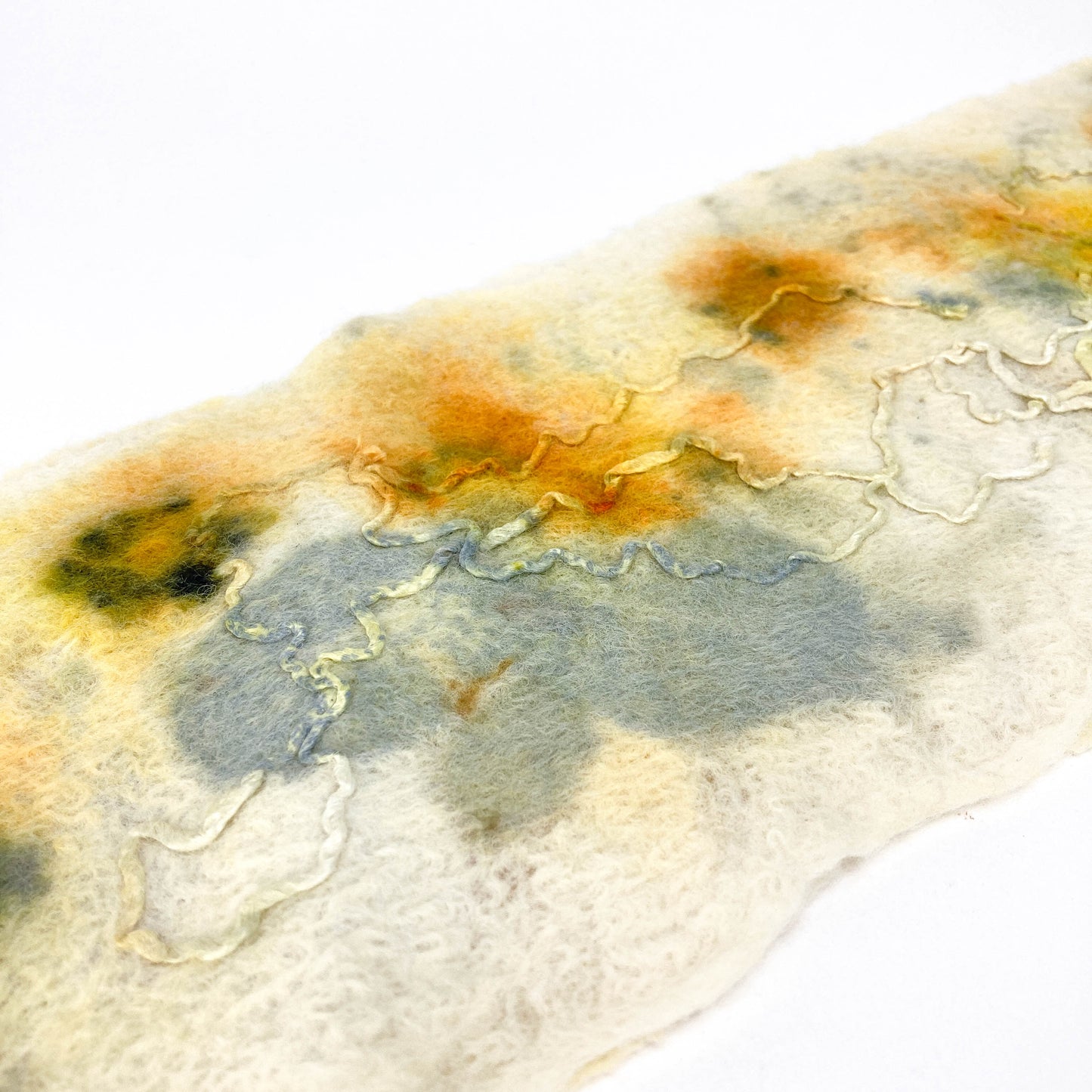 A textured, off-white Eco Print Scarf with abstract botanical dye patterns in muted orange, yellow, and gray hues.