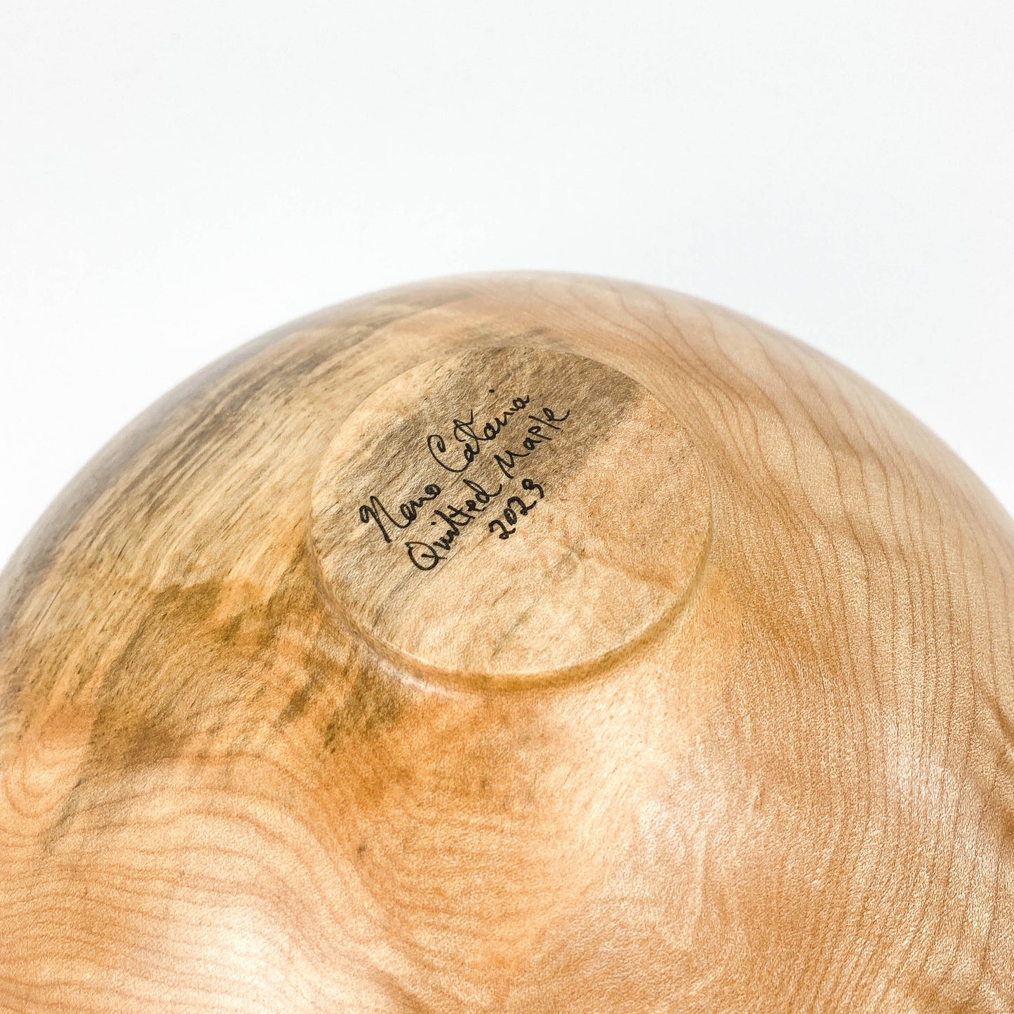 Close-up of the base of a quilted maple bowl with an inscription "Neno Catania Quilted Maple 2023".