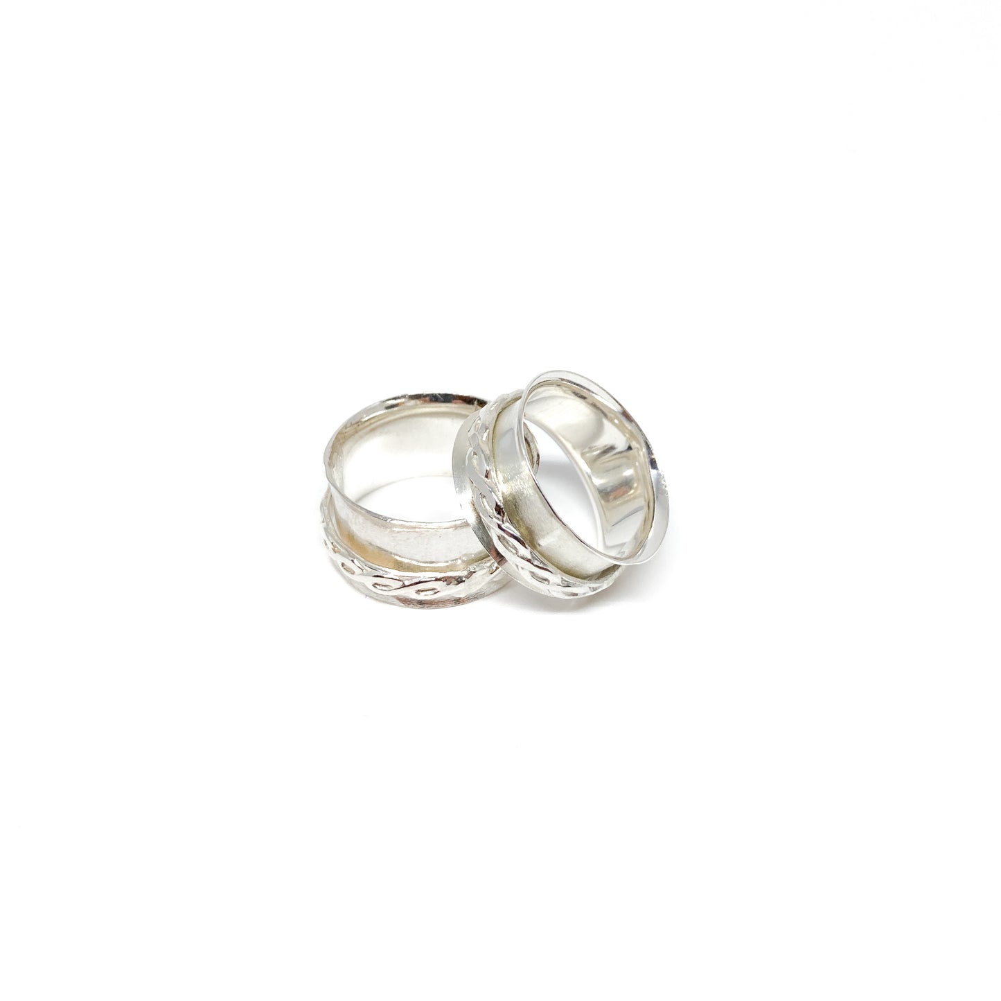 Two silver spinner rings with textured bands, one with a swirling pattern, resting on each other.