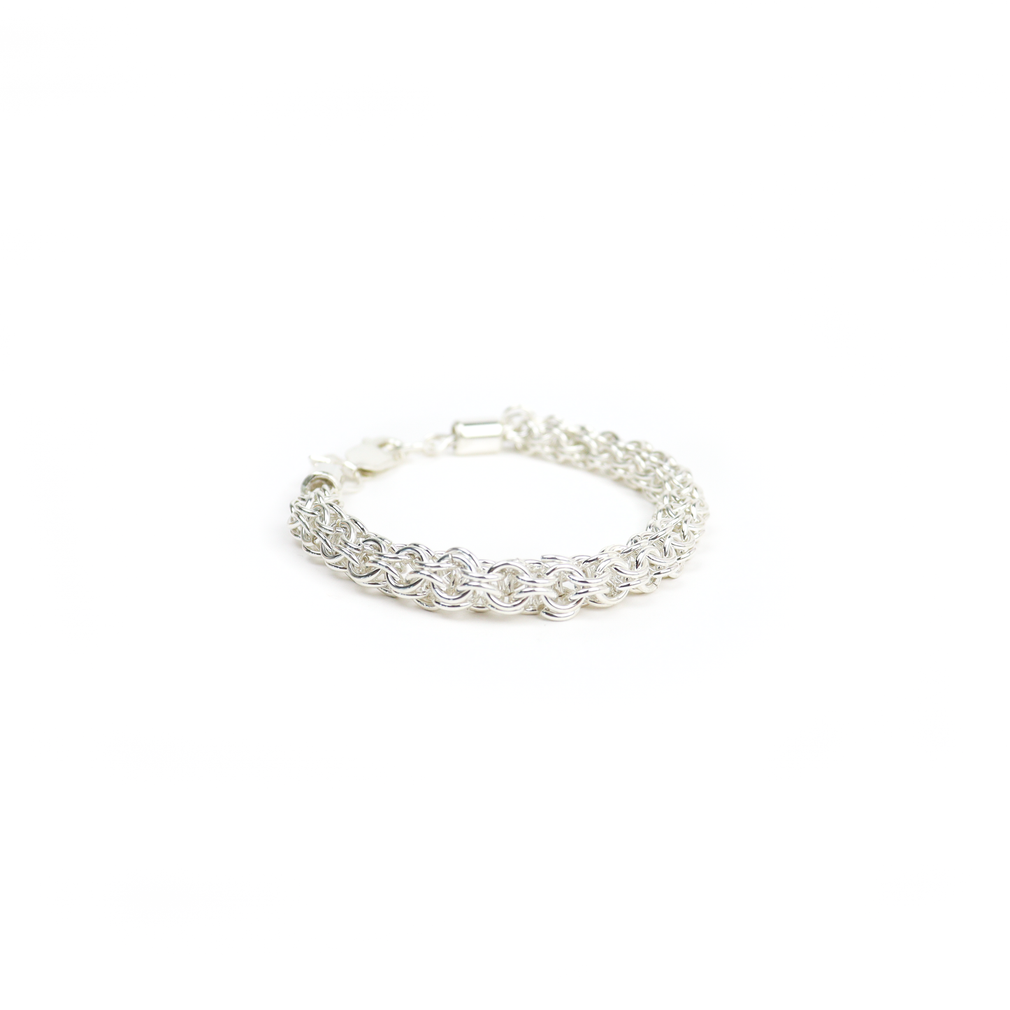 Thick silver Chain Mail Bracelet placed on a wooden surface, showing intricate woven design.