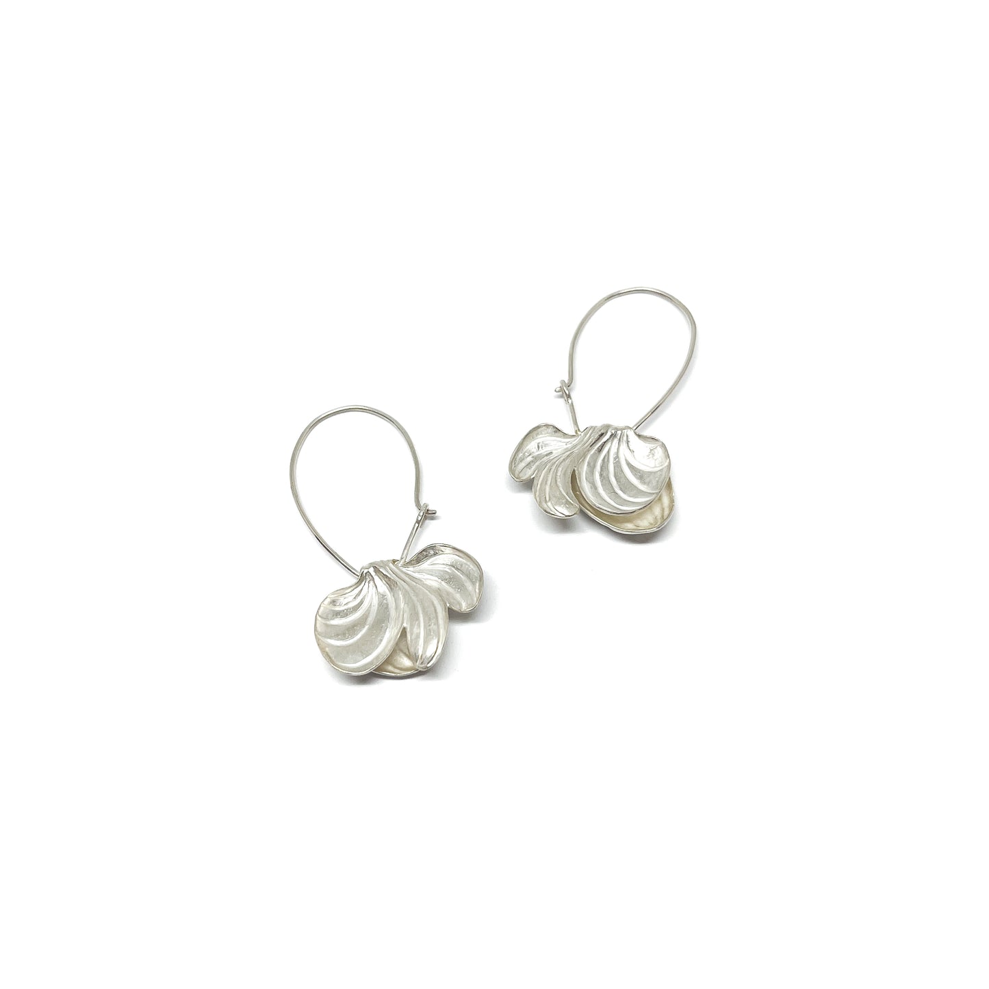 A pair of silver hoop earrings with textured, stylized calla lily or shell-like pendants dangling from the delicate loops.