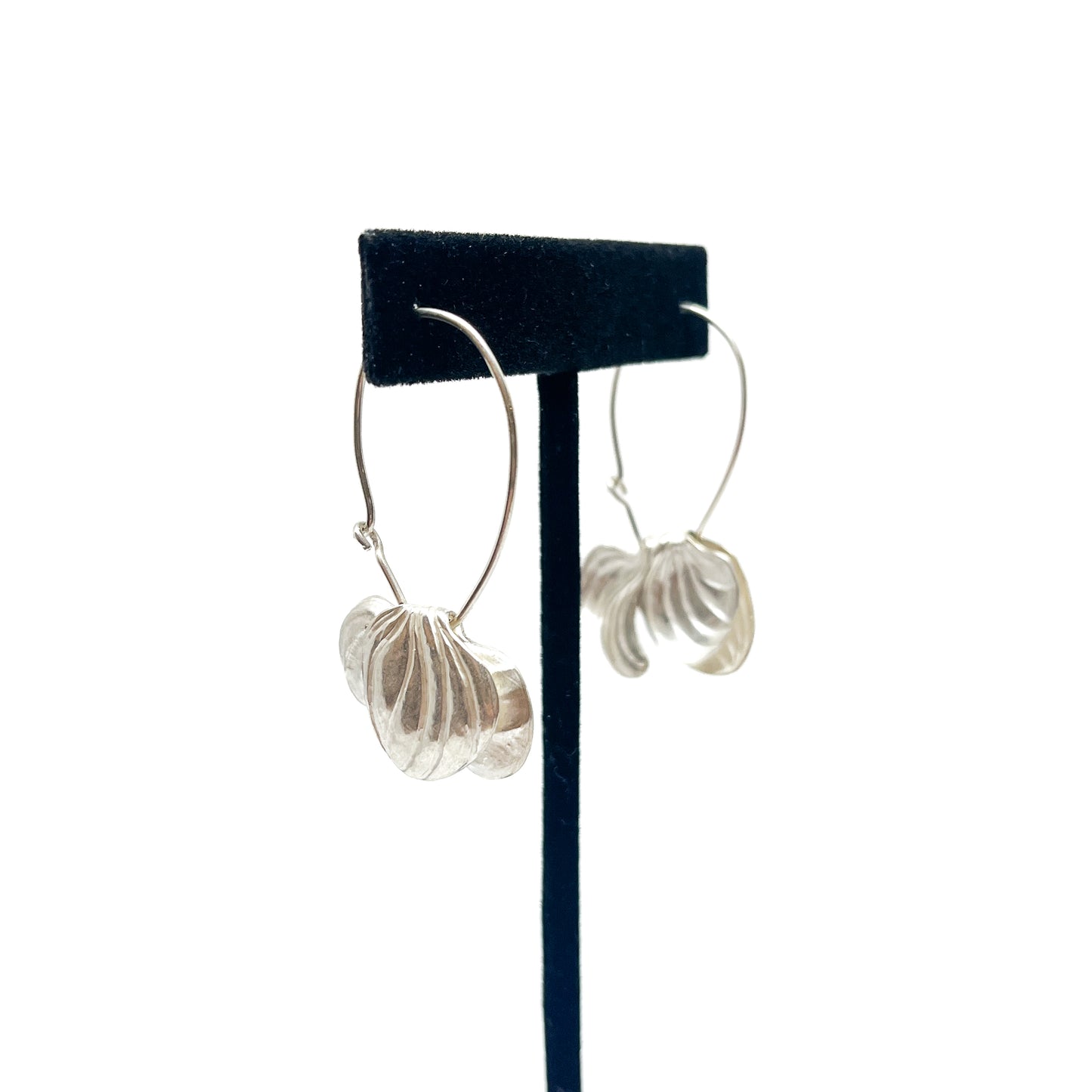 A pair of silver hoop earrings on a black display stand. Each earring features textured, abstract floral or shell-like pendants.