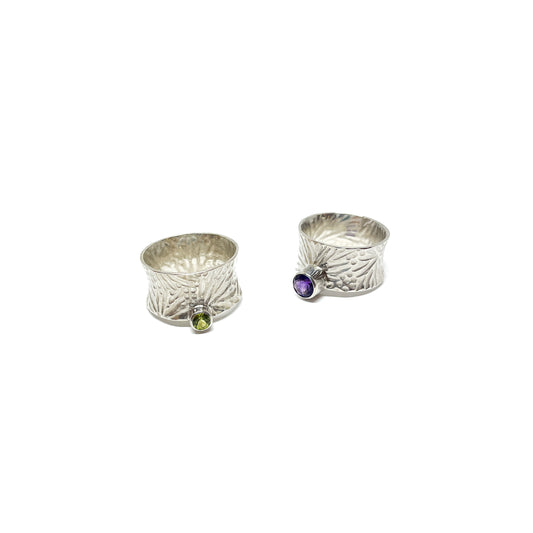 Two textured sterling silver spinner rings. One features a peridot, the other an amethyst gemstone.