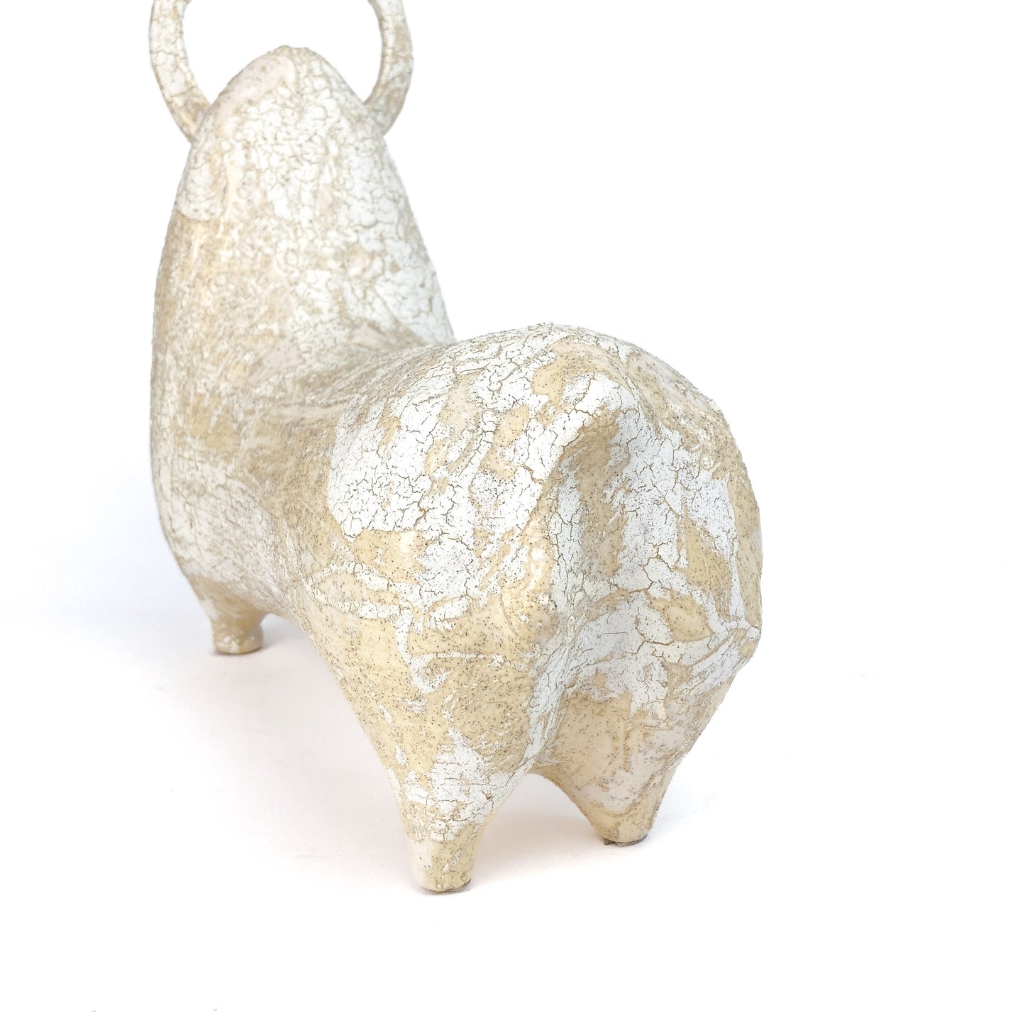 Rear view of a textured, light-toned ceramic bull figurine with small horns and a raised tail, showing a crackled glaze.