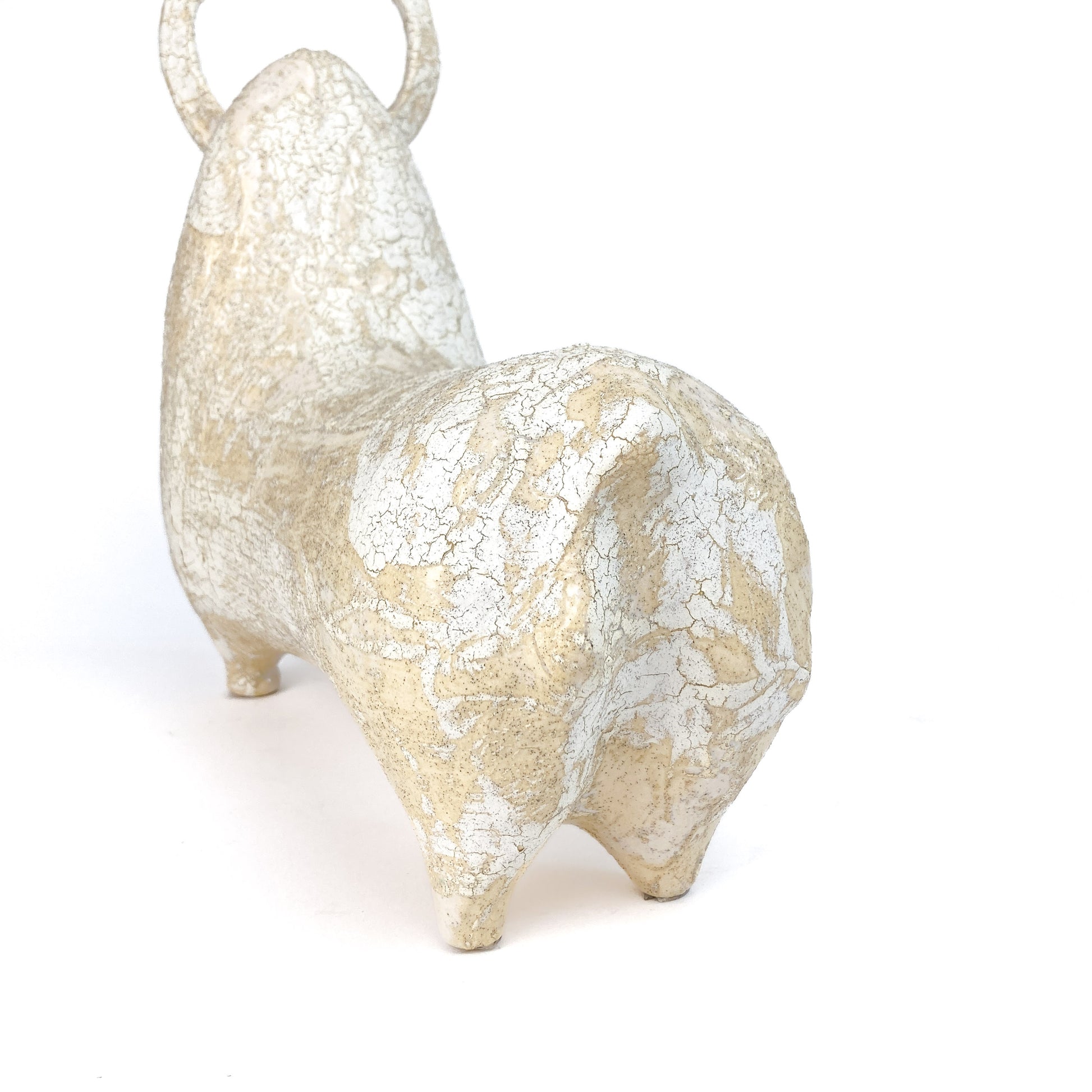 Rear view of a textured, light-toned ceramic bull figurine with small horns and a raised tail, showing a crackled glaze.