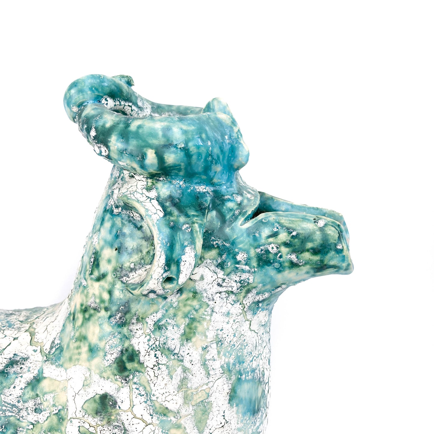 Close-up of a textured ceramic bull head with a teal and white mottled glaze and curled horns.