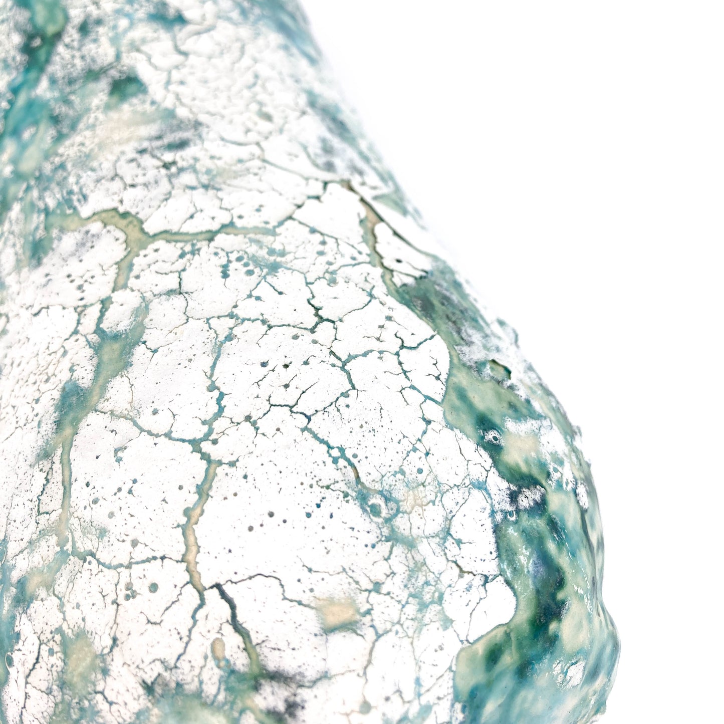 Close-up of a textured ceramic surface with a cracked, mottled teal and white glaze.