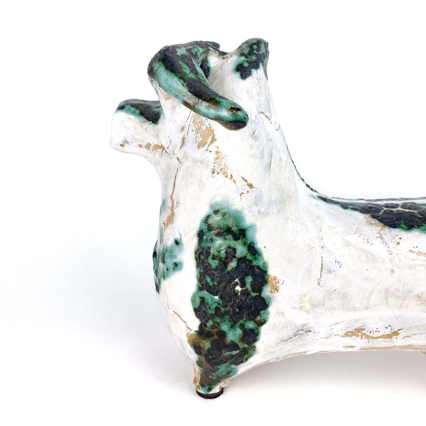 Partial view of a textured ceramic bull figurine with white, teal, and black mottled markings and curled horns.