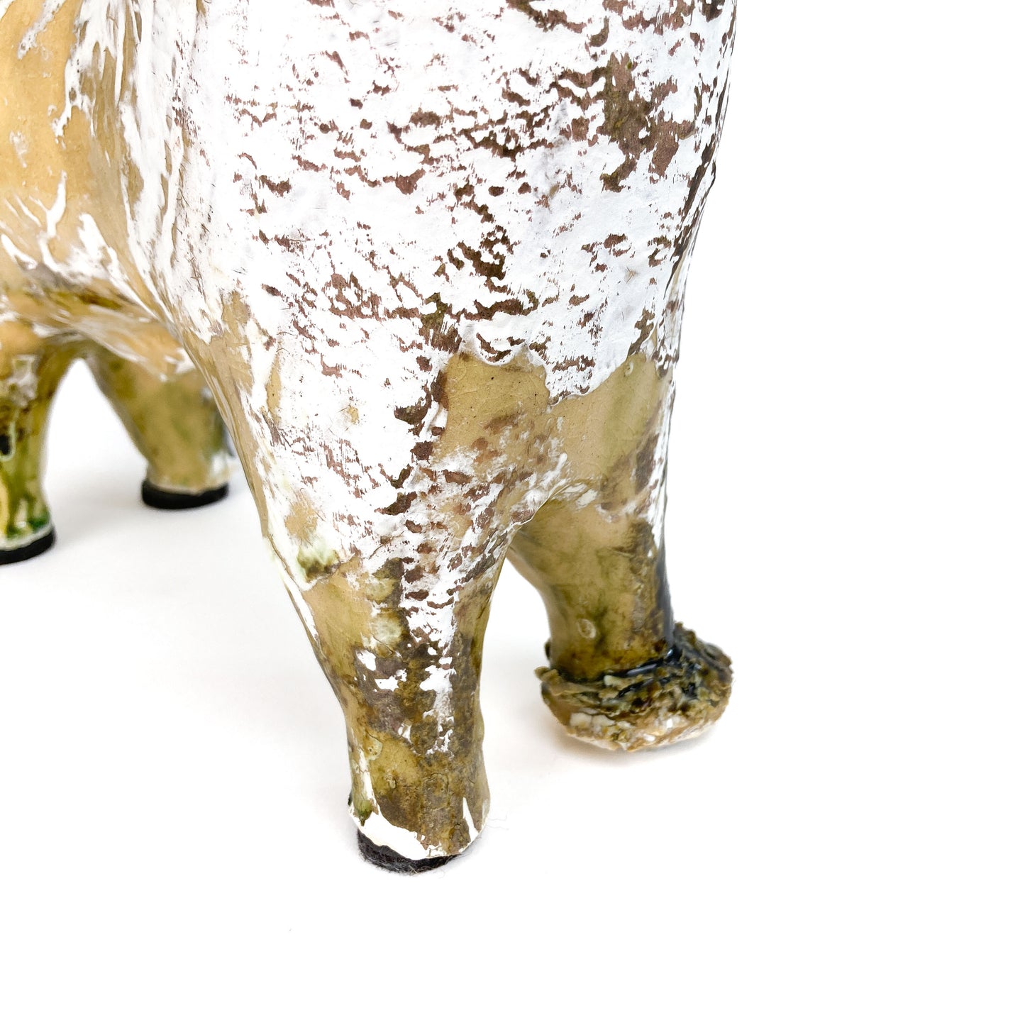 Close-up of the textured legs and hooves of a ceramic Long Neck Bull sculpture with a distressed light-toned glaze and white accents.