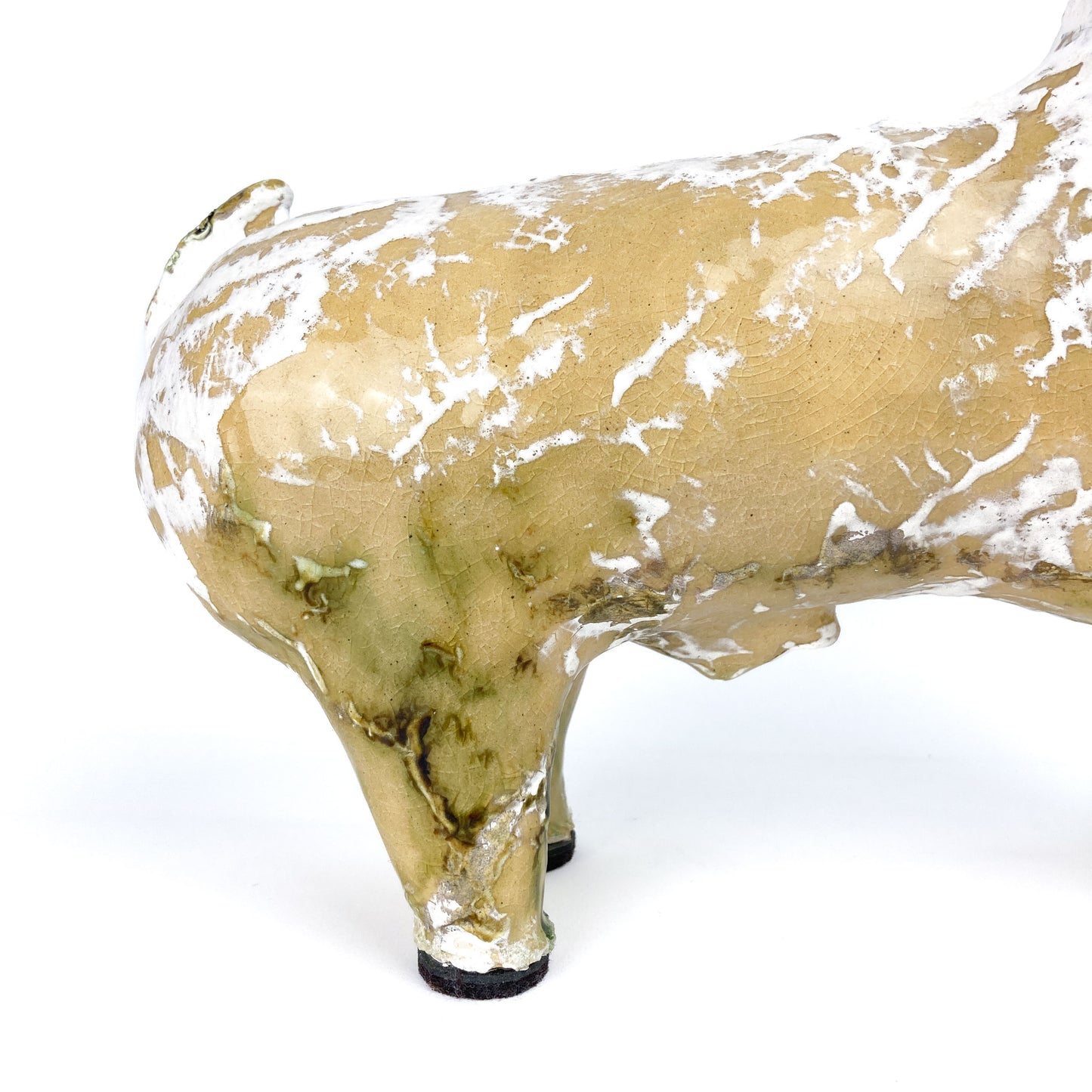 Partial view of a textured ceramic Long Neck Bull sculpture's rear leg and body with a distressed light-toned glaze and white accents.