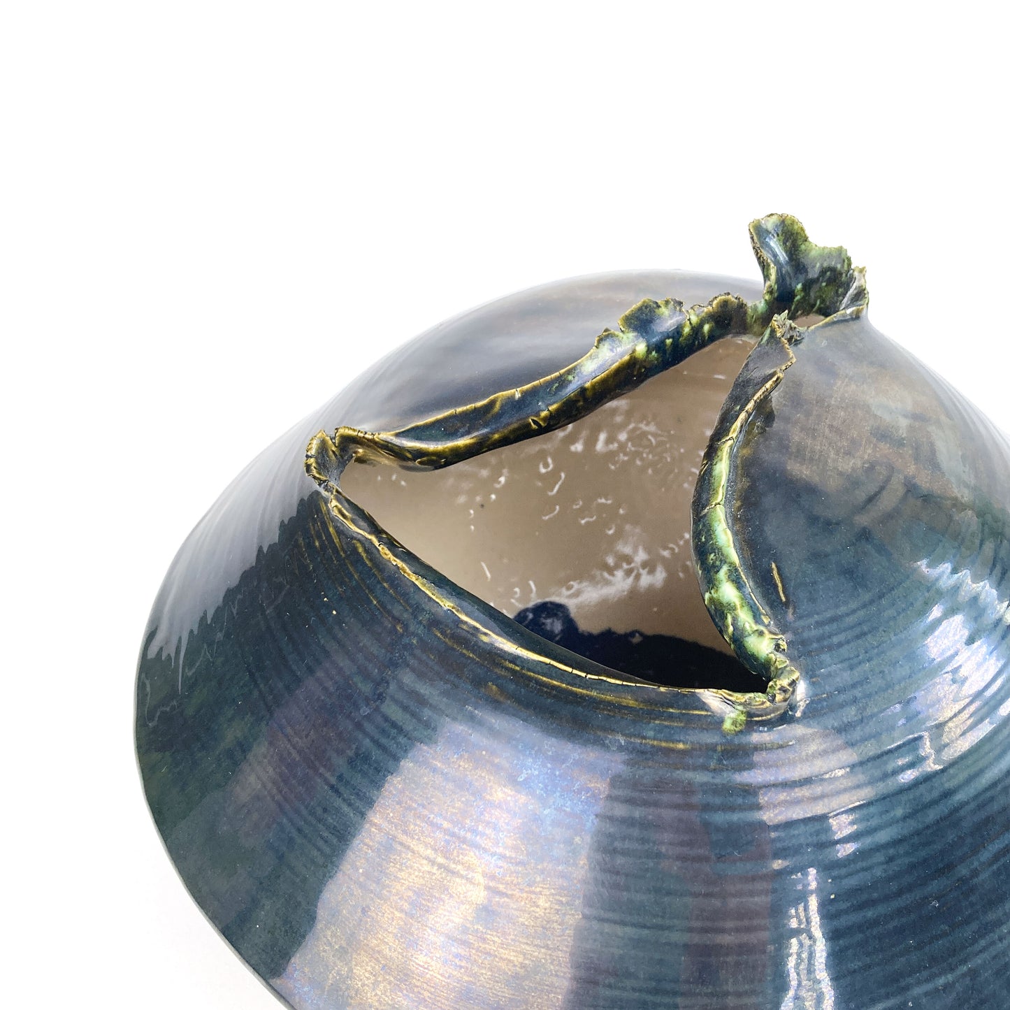 Close-up of a dark, round ceramic UFO sculpture showing a textured, jagged opening and a lighter-toned interior.