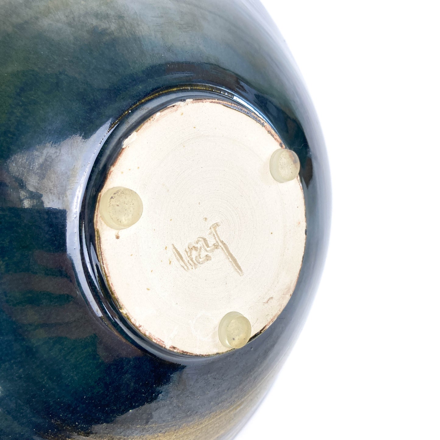 Bottom view of a dark ceramic UFO sculpture revealing a signature and three small, clear feet.