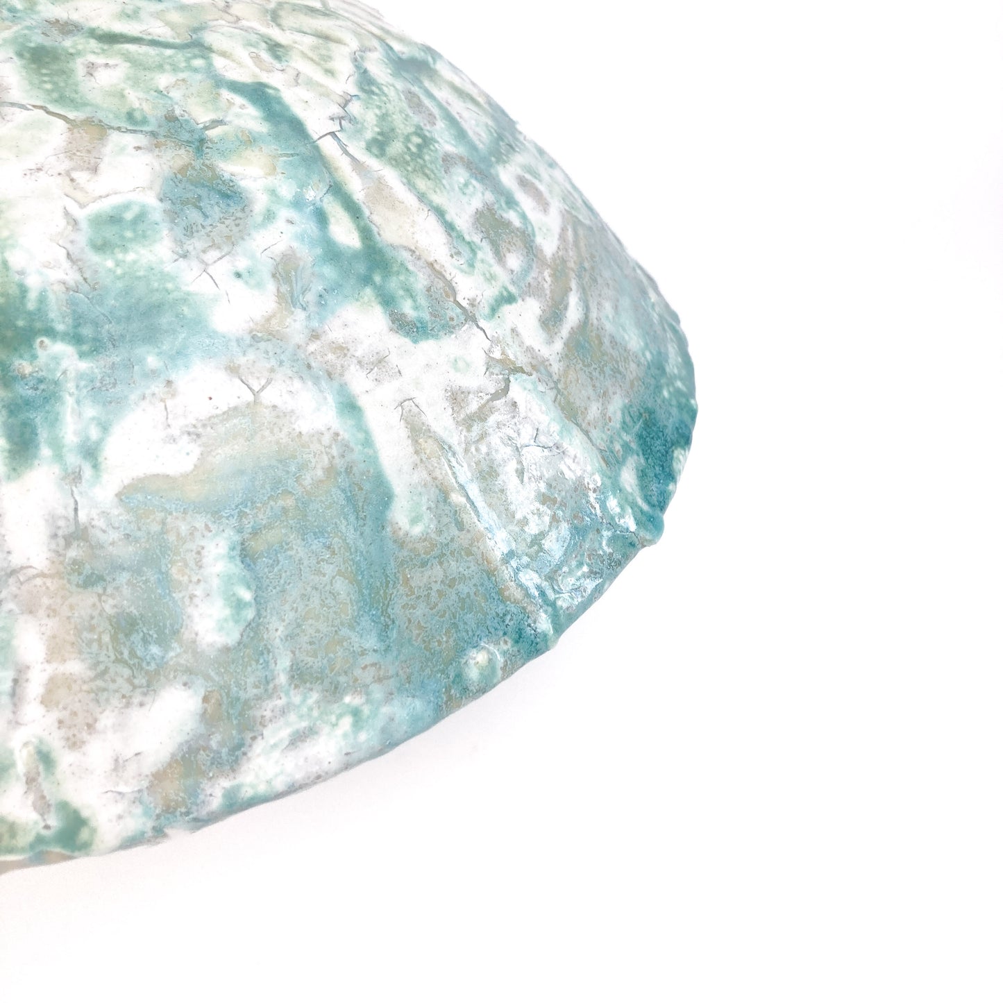 Close-up of the textured surface of a ceramic UFO vessel with a mottled teal and light beige crackled glaze.