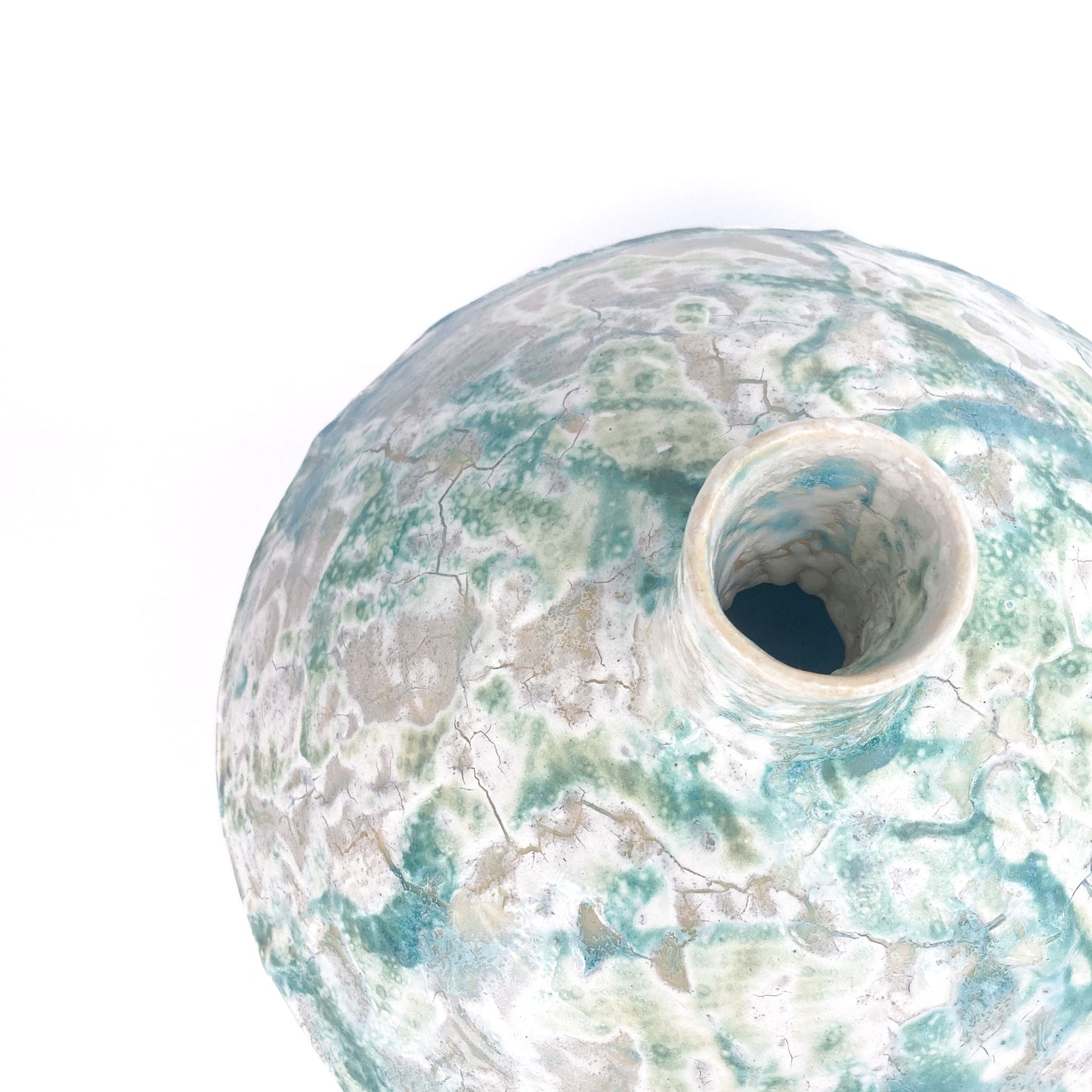 Close-up, angled view of the opening of a textured ceramic UFO vessel with a mottled teal and light beige crackled glaze.