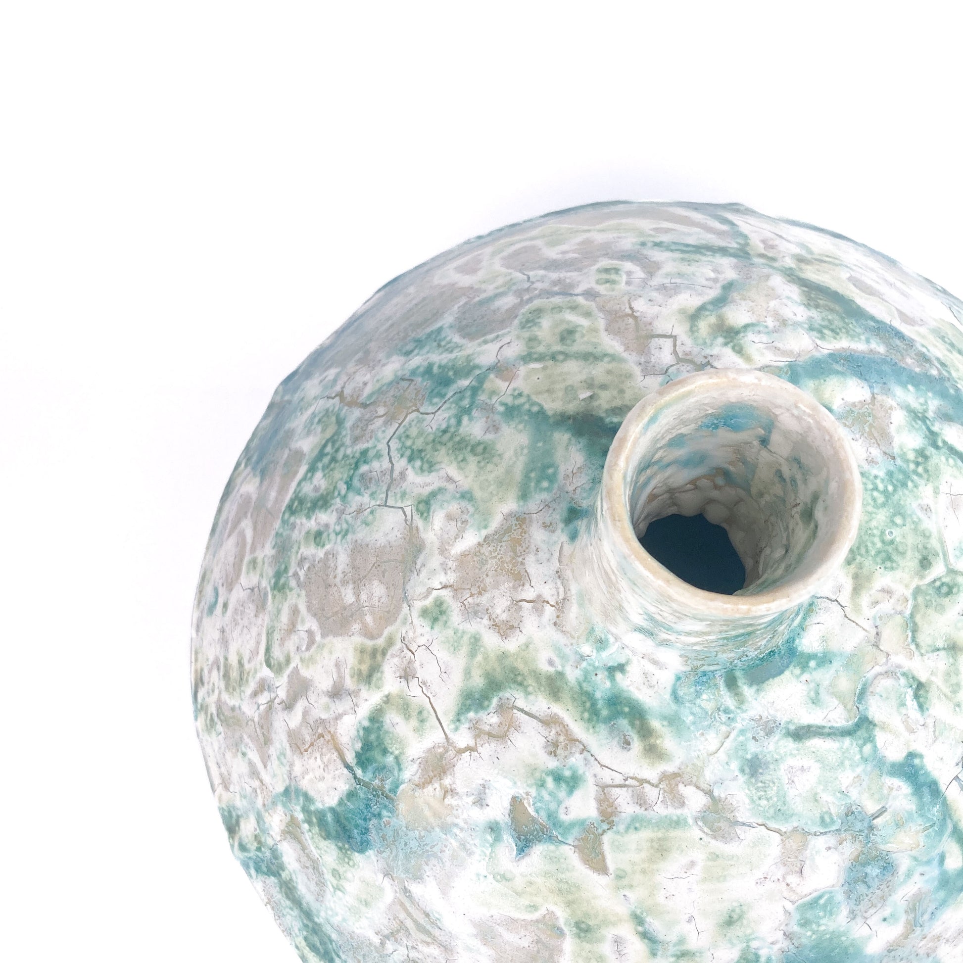 Close-up, angled view of the opening of a textured ceramic UFO vessel with a mottled teal and light beige crackled glaze.