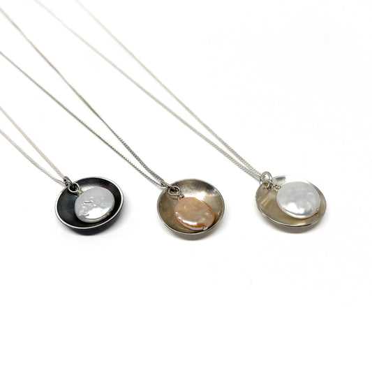 Three Pearl Disk Pendant Necklaces displayed side by side, each featuring a unique pearl and metal finish.