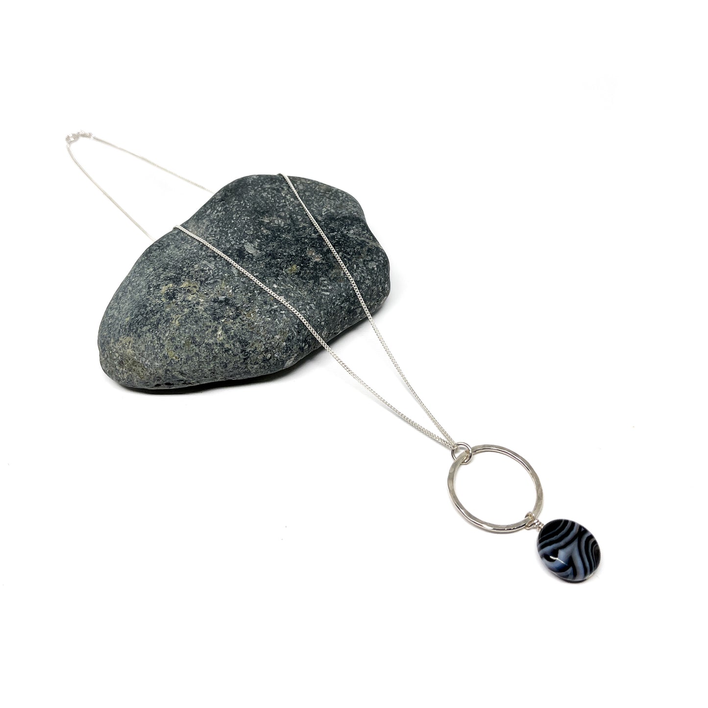 Silver loop pendant necklace with a striped black and white gem, resting on a stone.