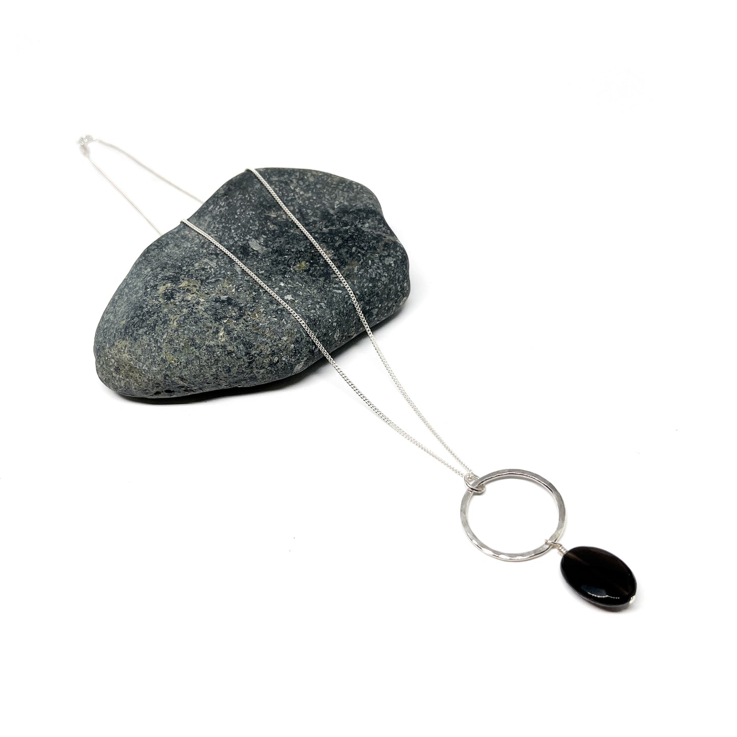 Silver loop pendant necklace with a solid black oval gem, displayed on a textured stone.
