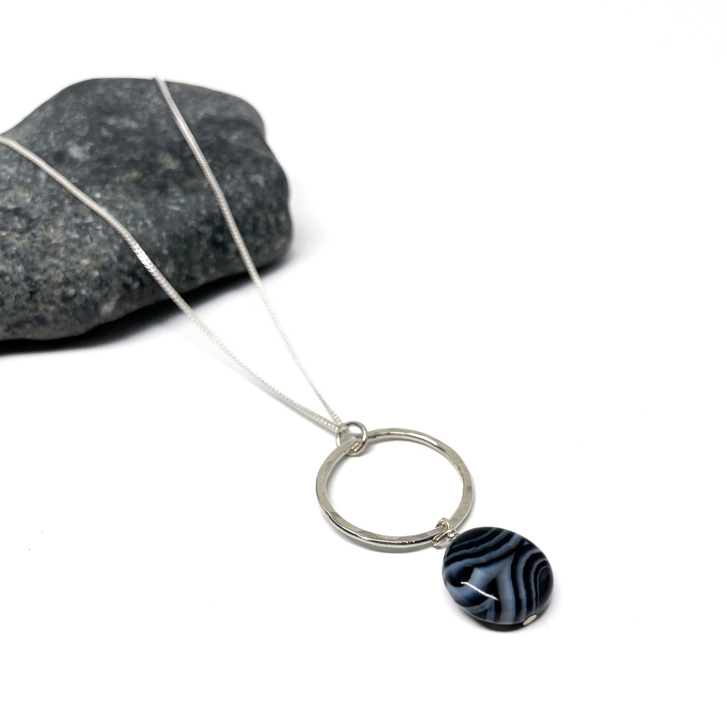 Close-up of a silver loop necklace with a striped black and white oval gem.