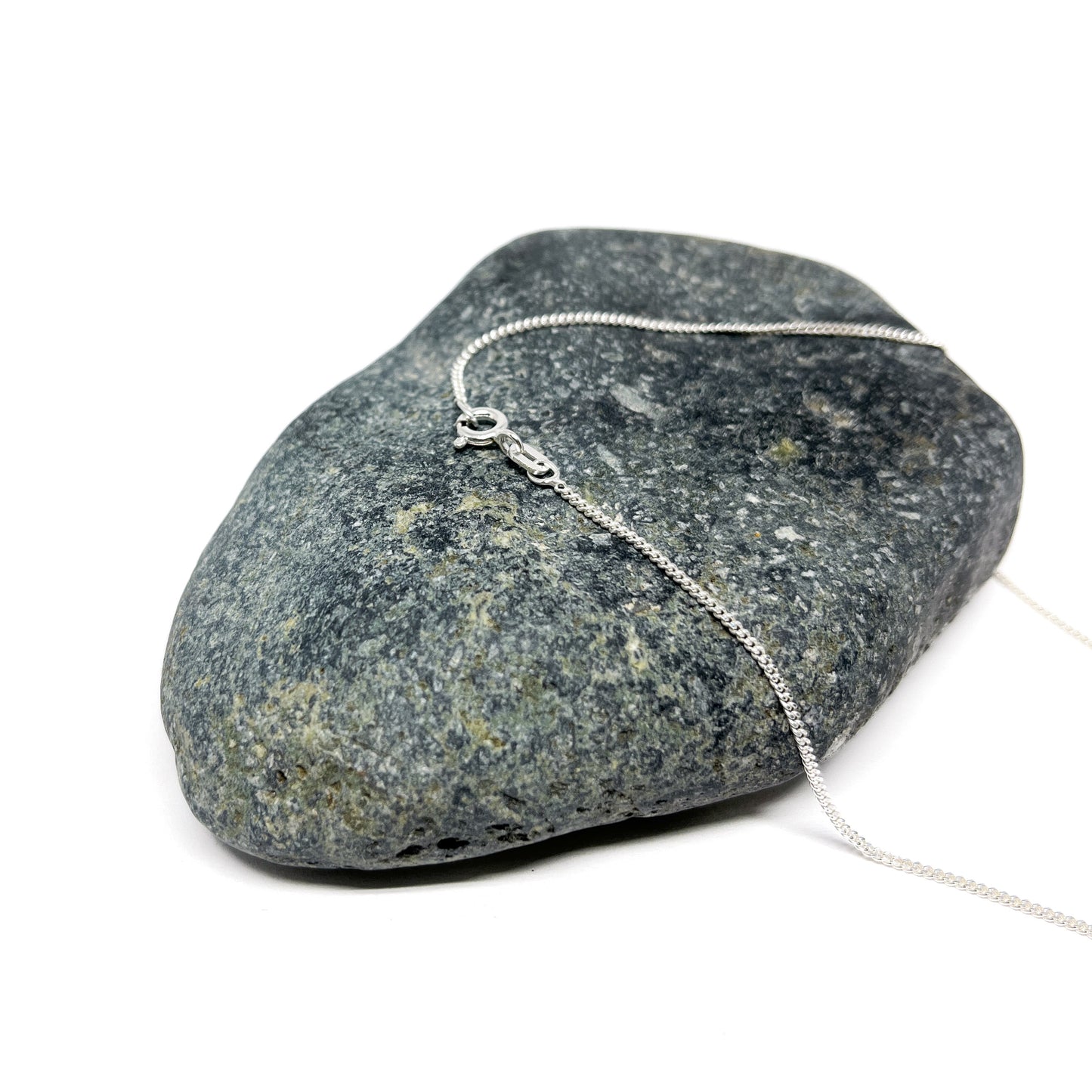 Close-up of the clasp of a silver chain necklace resting on a grey stone.